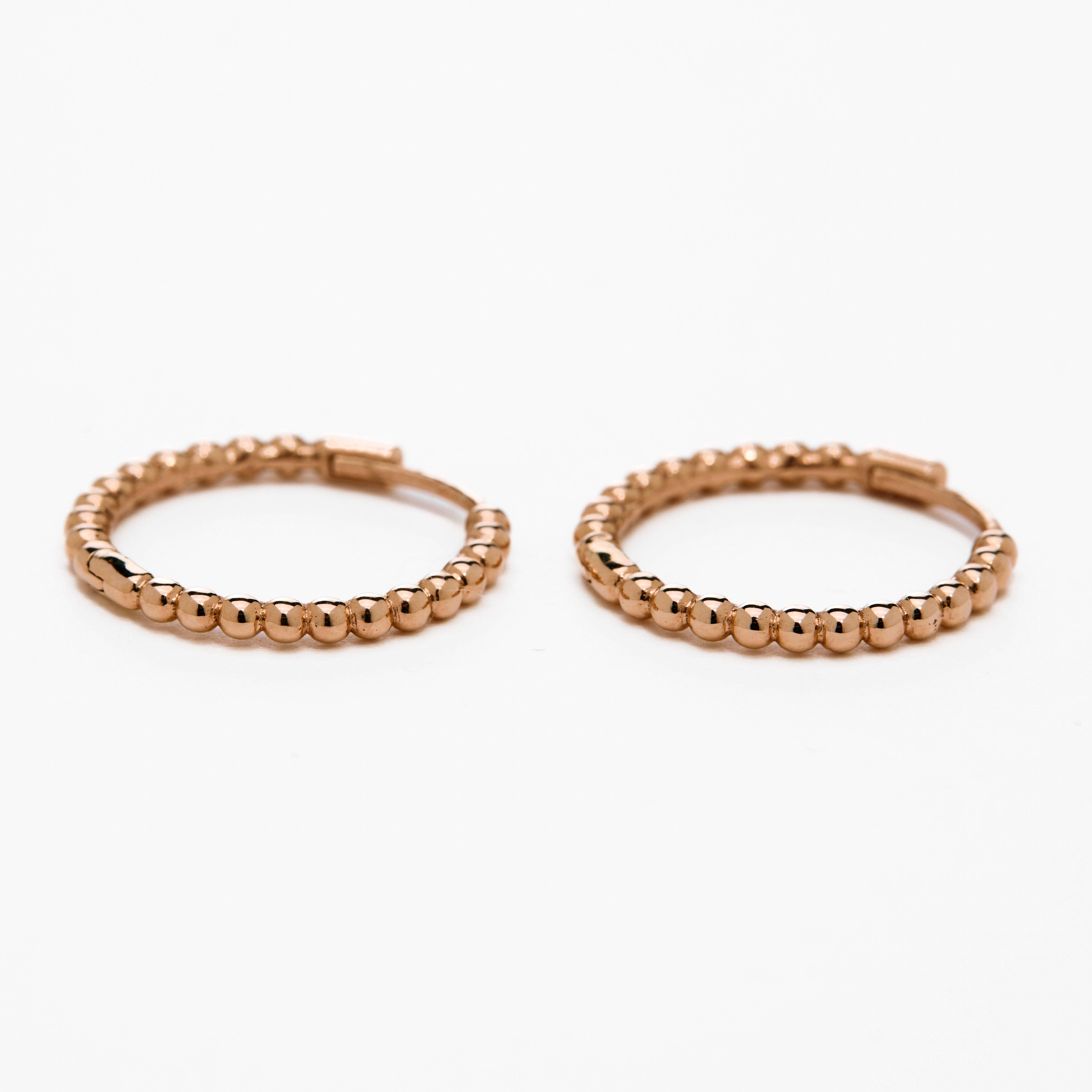 A pair of rose gold-colored hoop earrings with a textured surface, displayed against a white background.