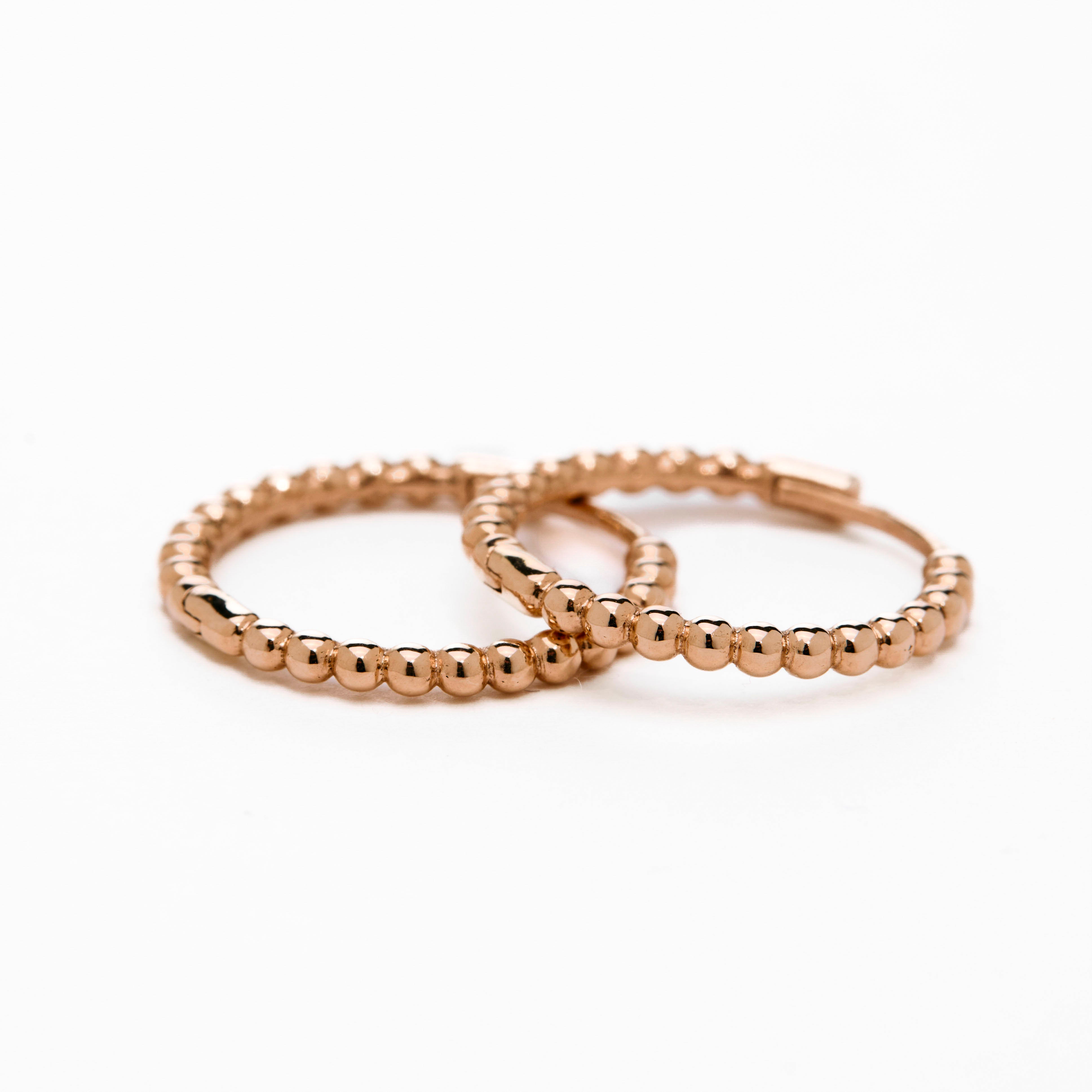 A pair of rose gold-colored hoop earrings with a textured surface, displayed against a white background.