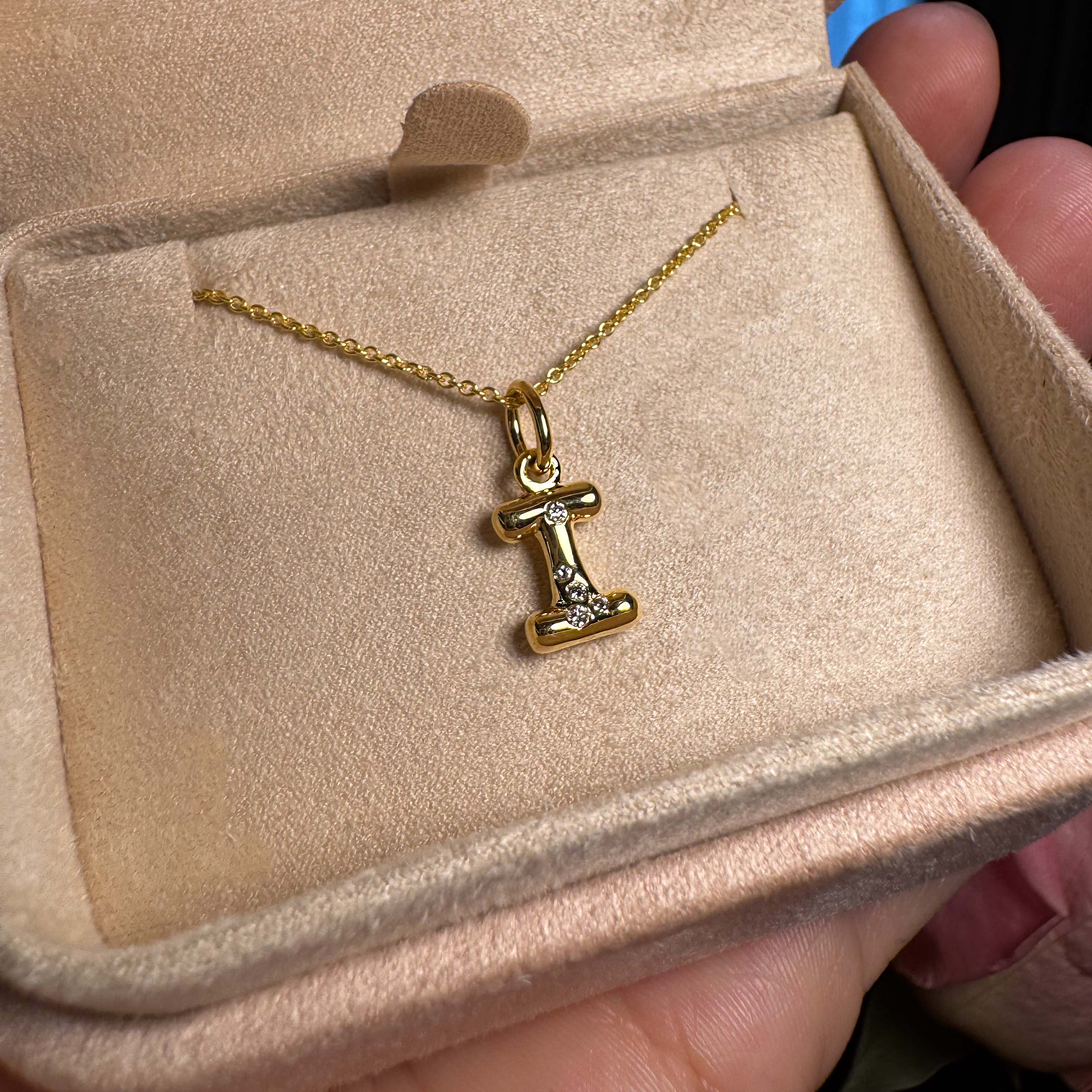 Gold necklace with a 'I' pendant in an open jewelry box.