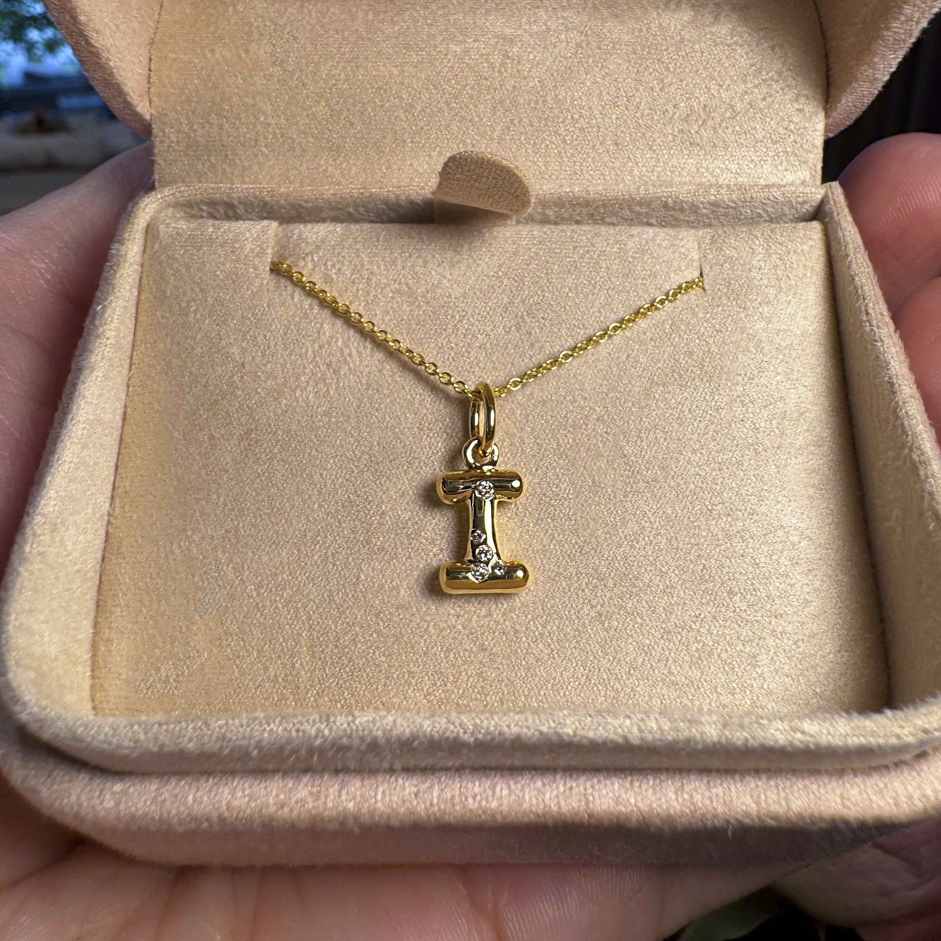 Gold necklace with a letter 'I' pendant in an open jewelry box.
