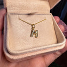 Gold diamonds necklace with a 'M' pendant in a jewelry box held by a hand.
