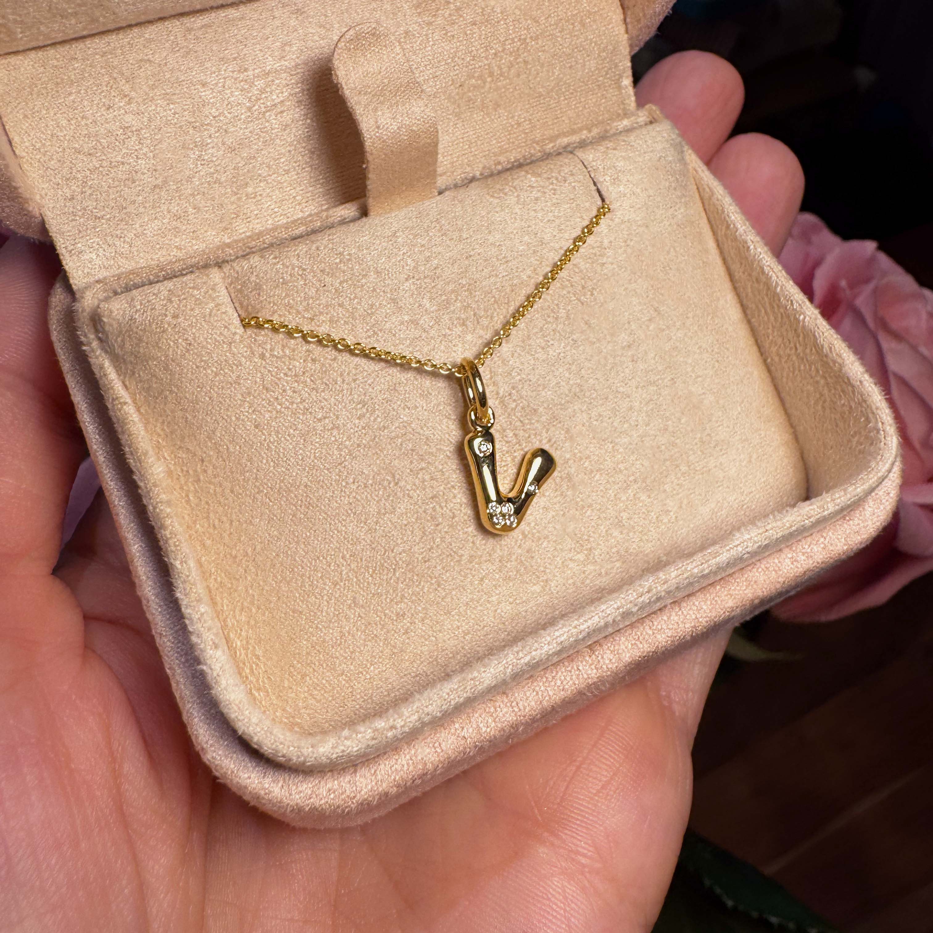 Gold necklace with a 'V' pendant in a beige jewelry box held by a hand.
