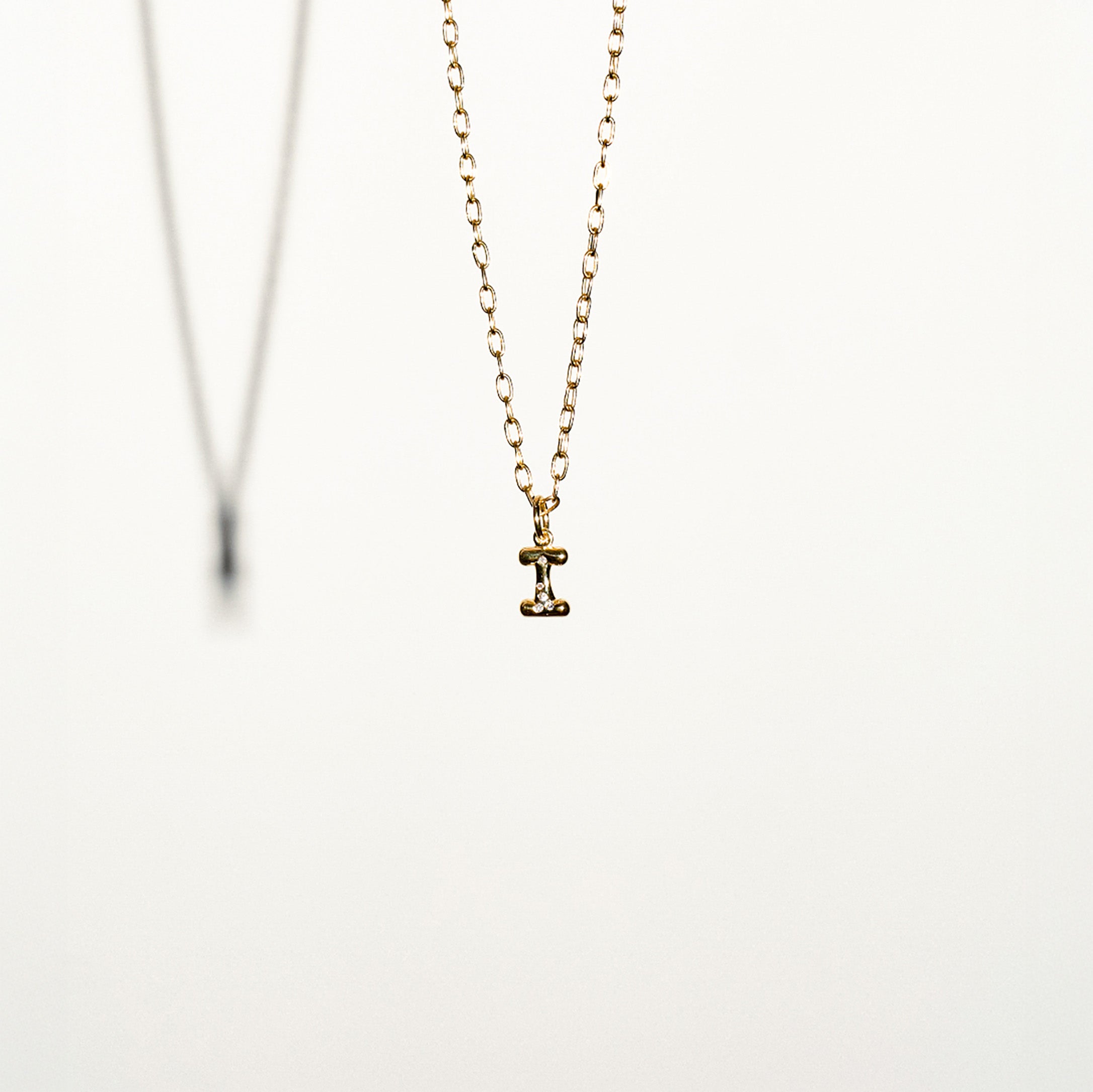 Gold necklace with a small I letter pendant on a white background