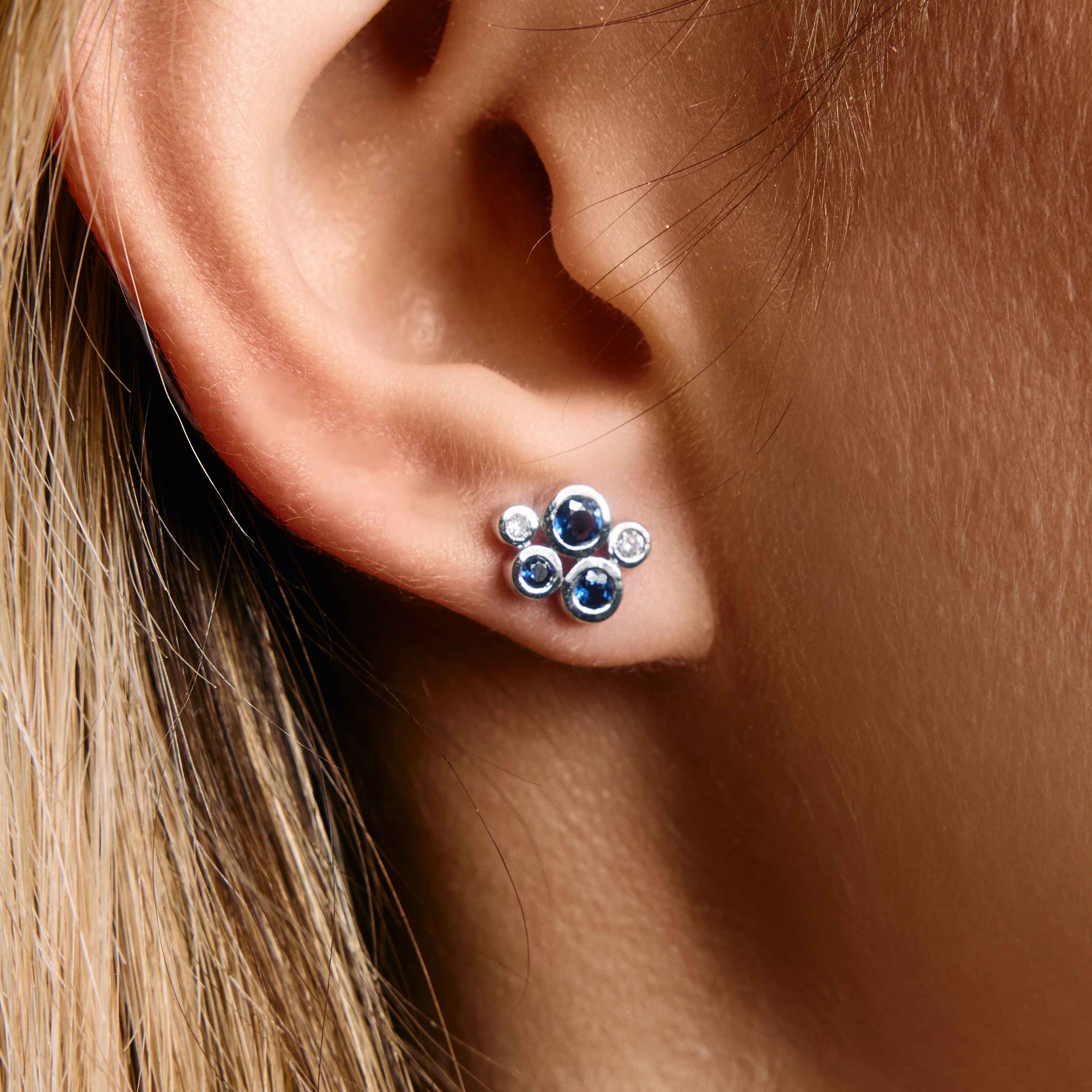 gold stud earrings with blue sapphires and white diamond cluster design on ear