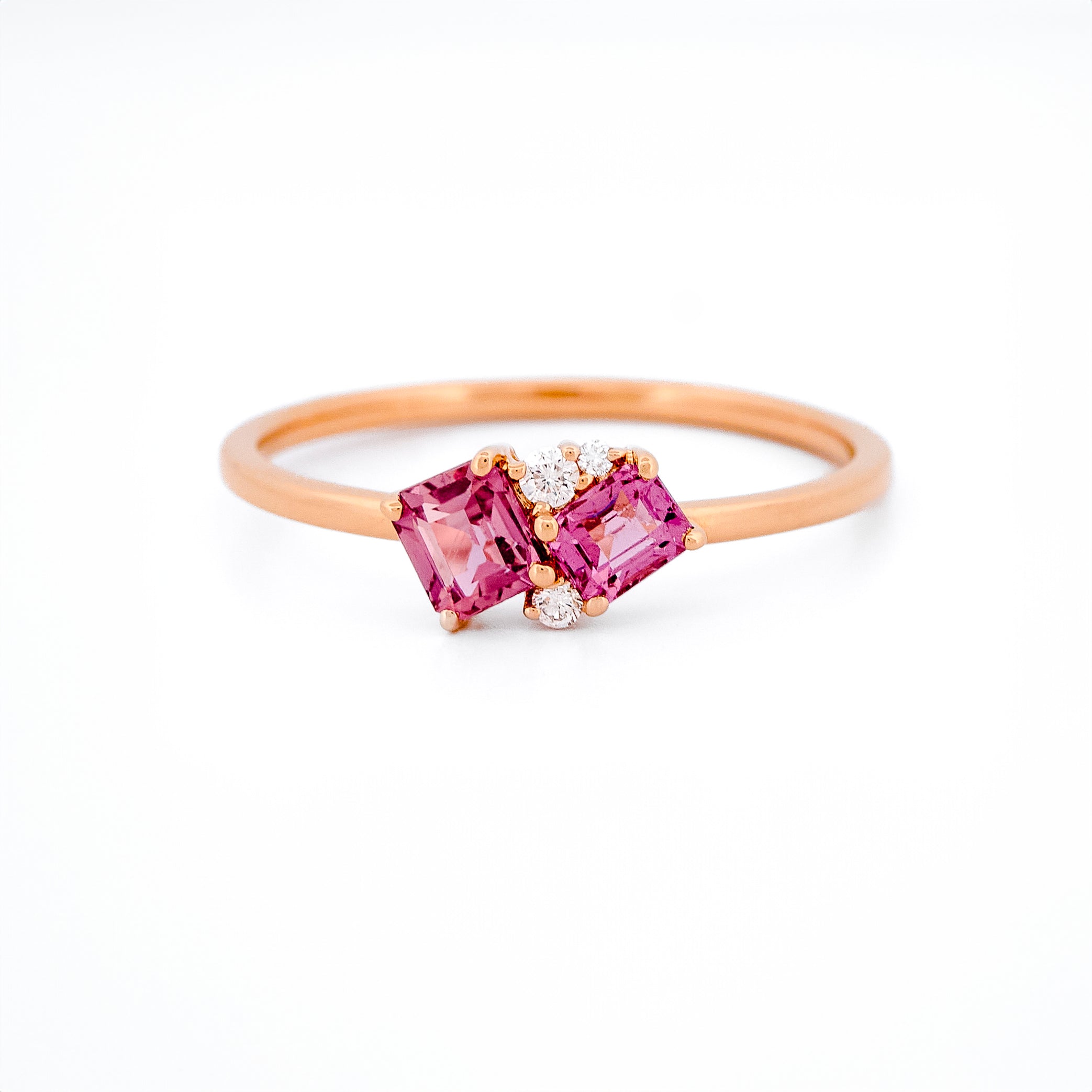 Gold ring with two pink sapphires and diamonds accents on a white background