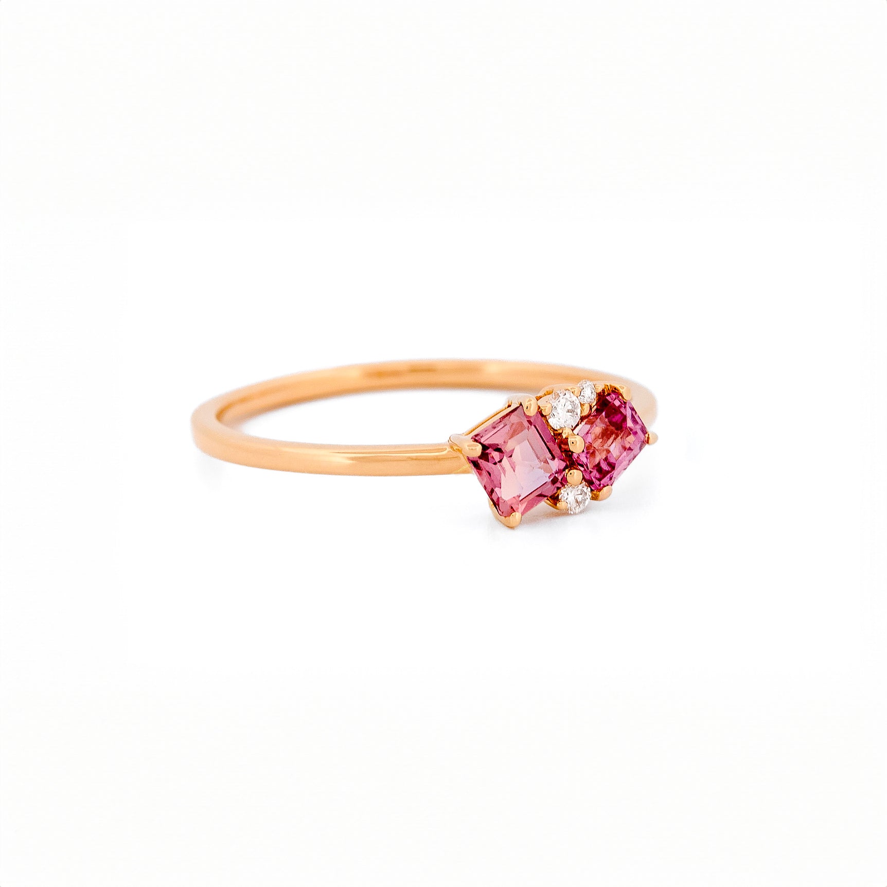 Gold ring with two pink sapphires and diamonds accents on a white background