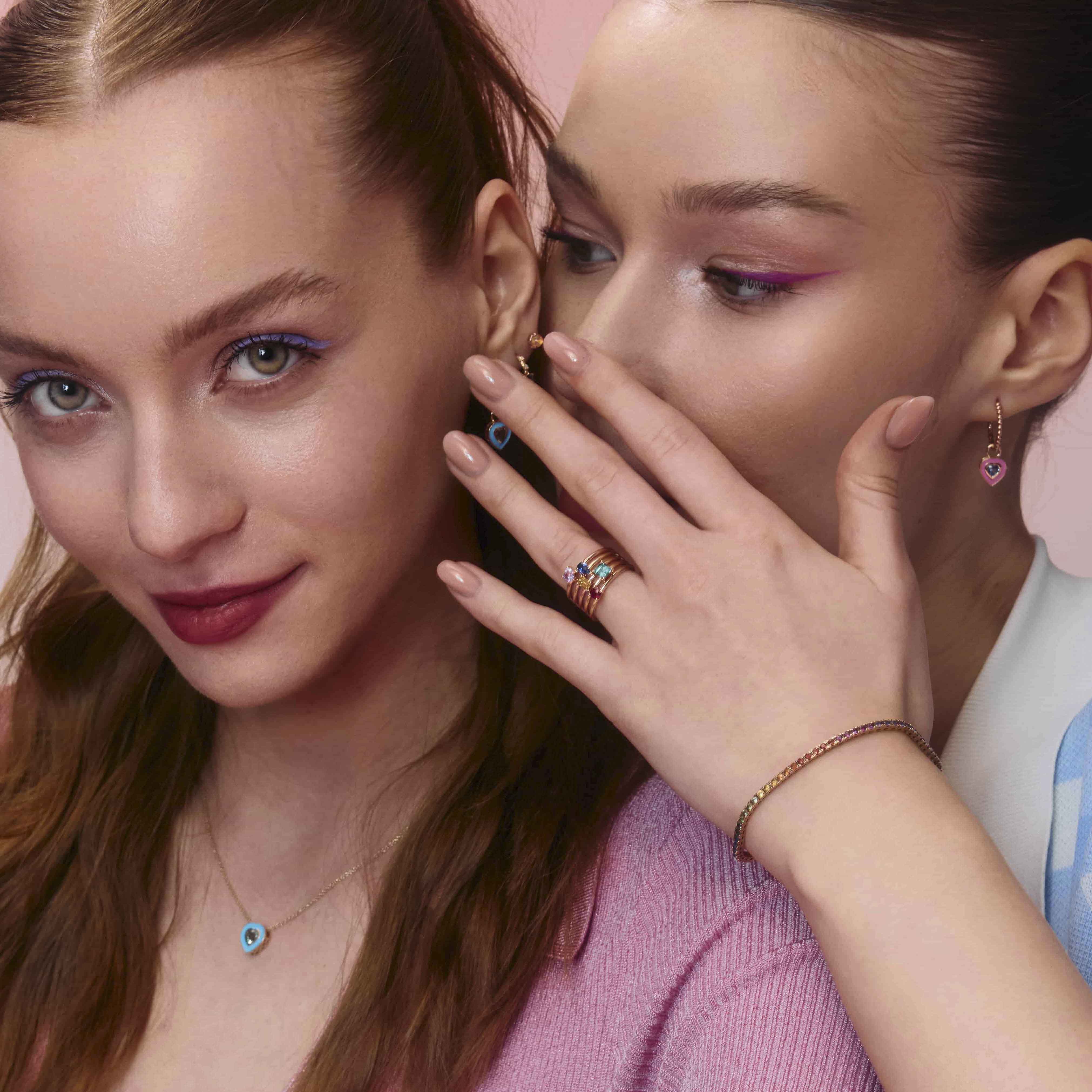 A pair of yellow  gold hoop earrings with a bubbly design, enamel heart earring accessories and mix and match rings, displayed on models.