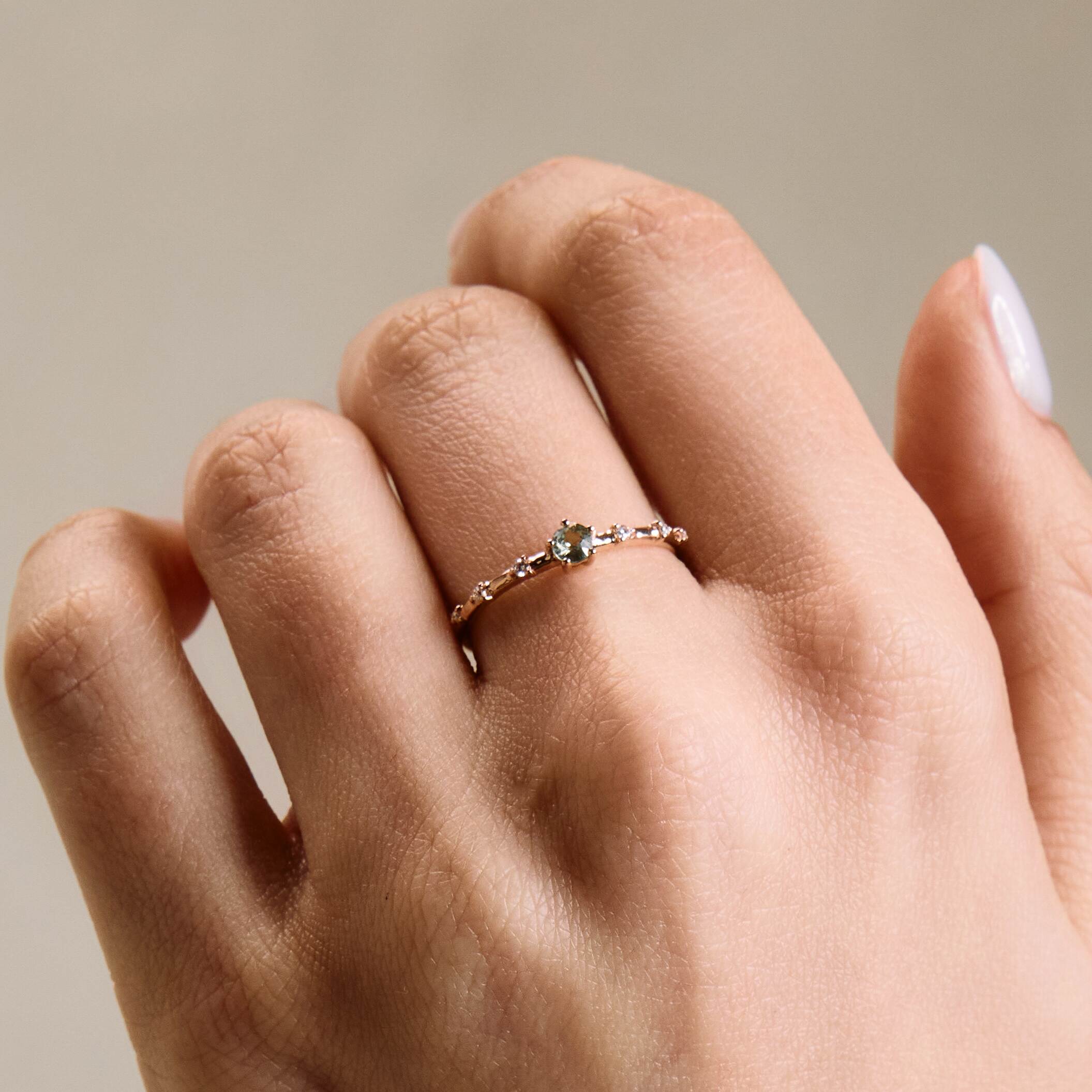 A gold band ring featuring a central sapphire with smaller diamond accents around it, presented on a hand