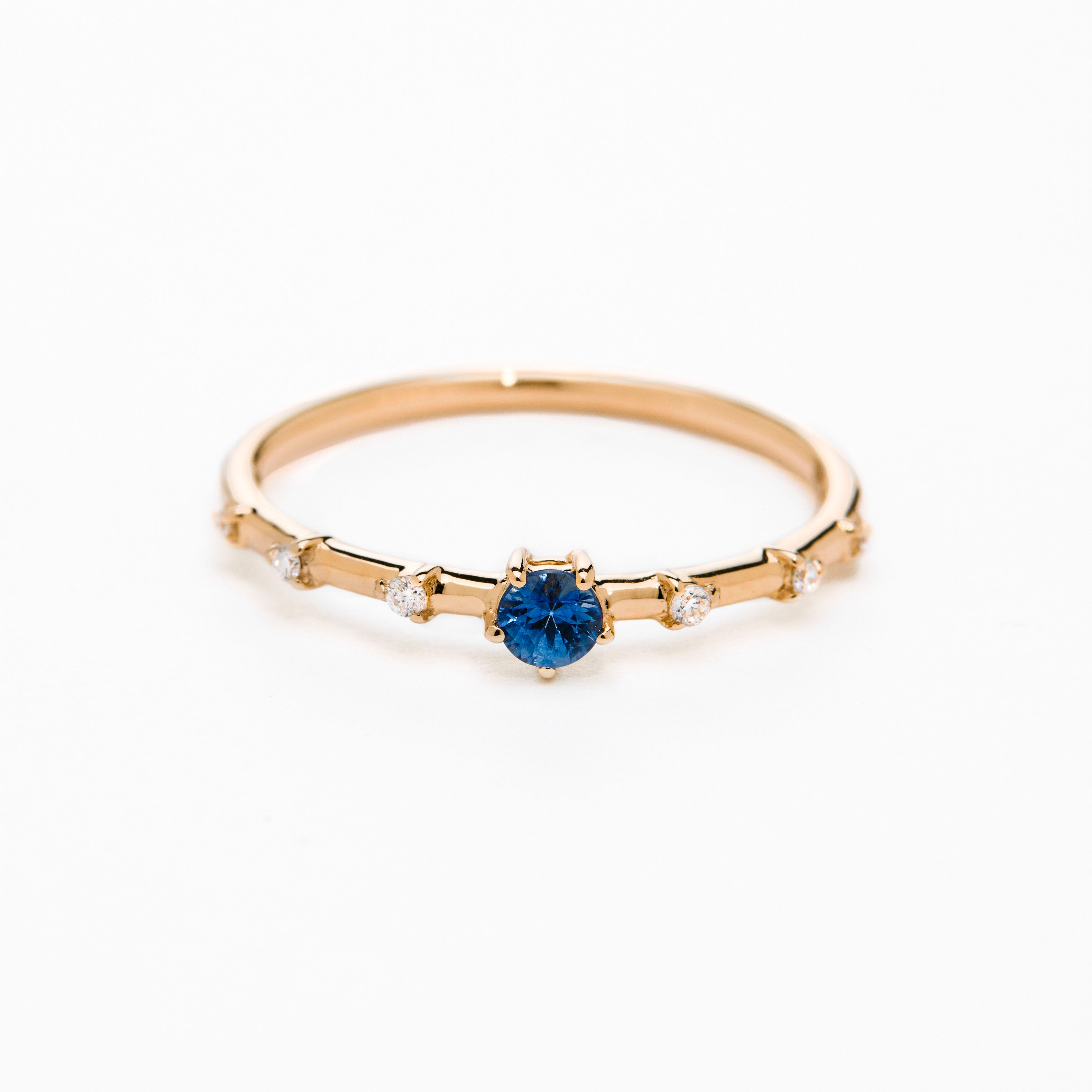 A gold band ring featuring a central sapphire with smaller diamond accents around it, presented against a white background.