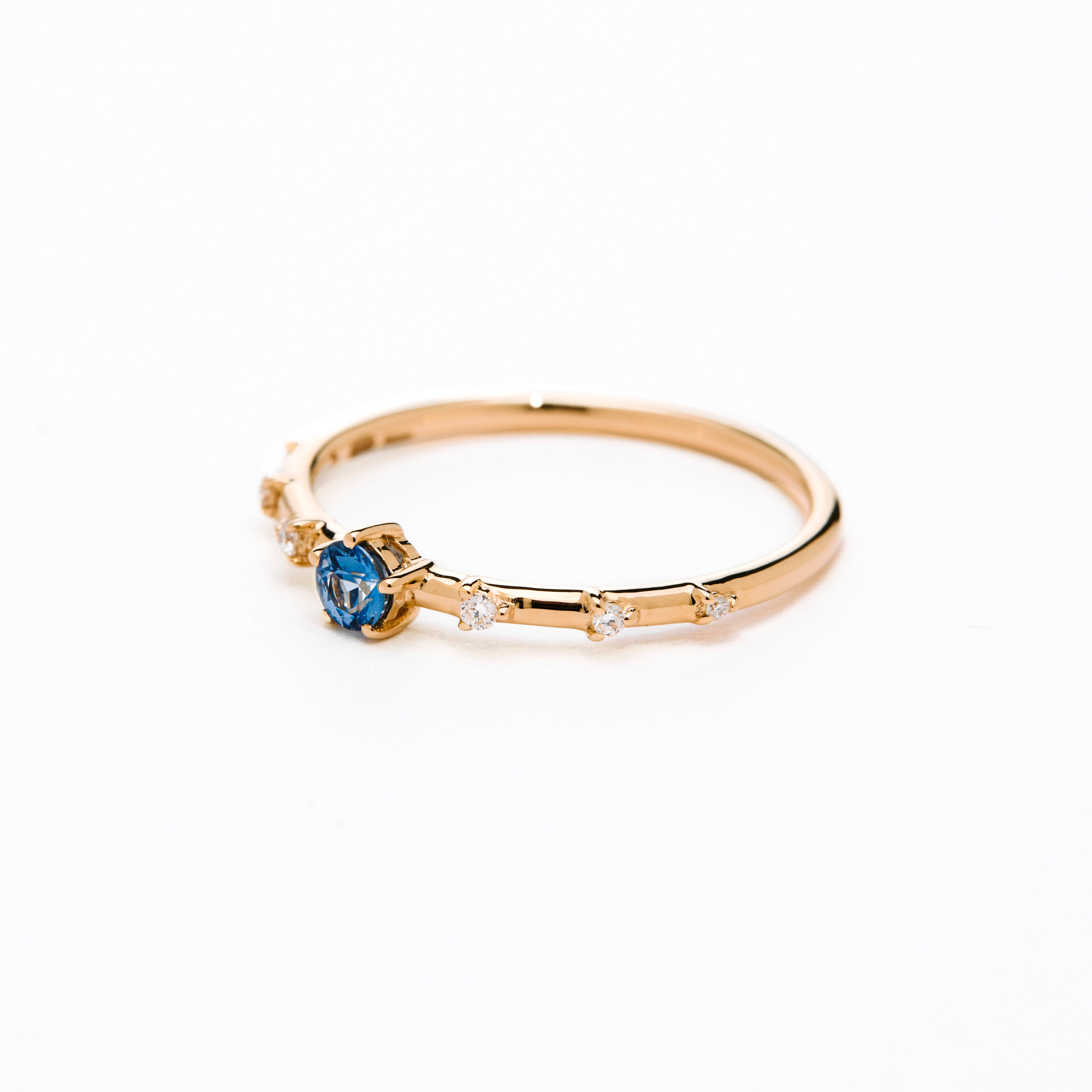 A gold band ring featuring a central sapphire with smaller diamond accents around it, presented against a white background.