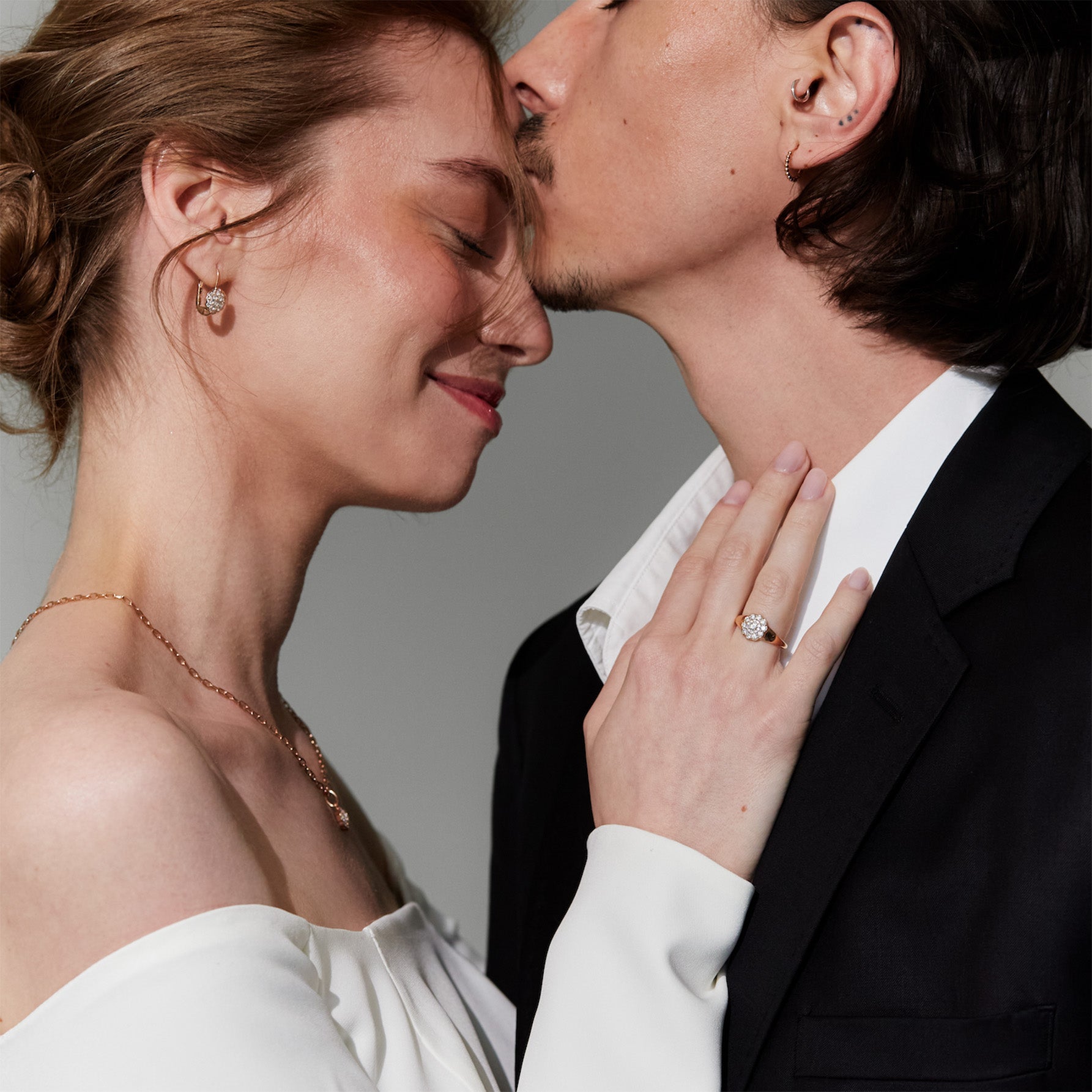 Close-up of a couple in wedding attire with a gray background, the woman is wearing daisies made of diamonds gold  jewelry. 
