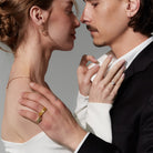 Close-up of a couple embracing with a gray background, They are both wearing diamonds and gold jewelry. 
