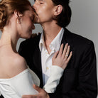 Two people embracing with a gray background, they are wearing elegant gold wedding jewelry