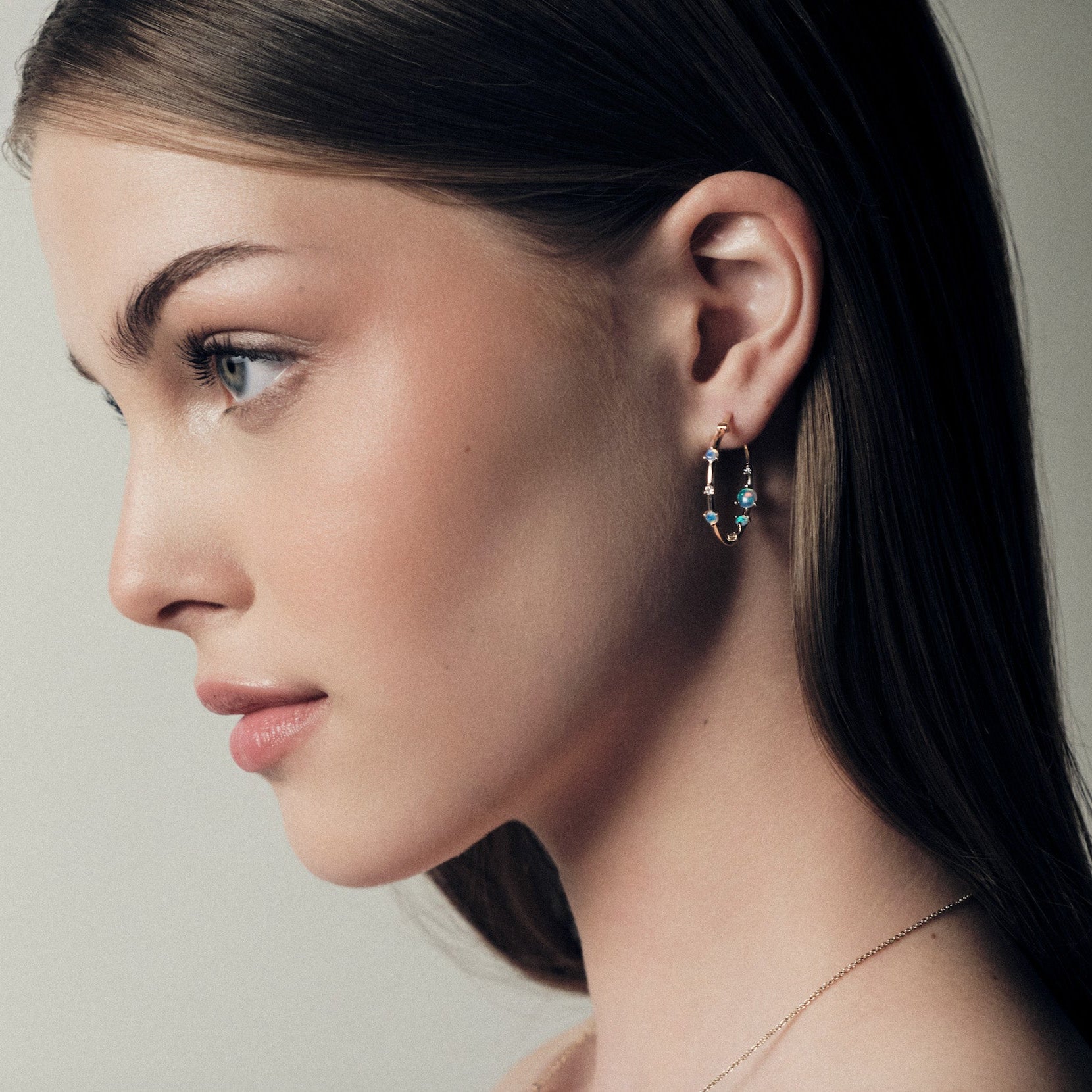 Close-up of a woman wearing australian opals 25mm hoop earrings with a neutral background.