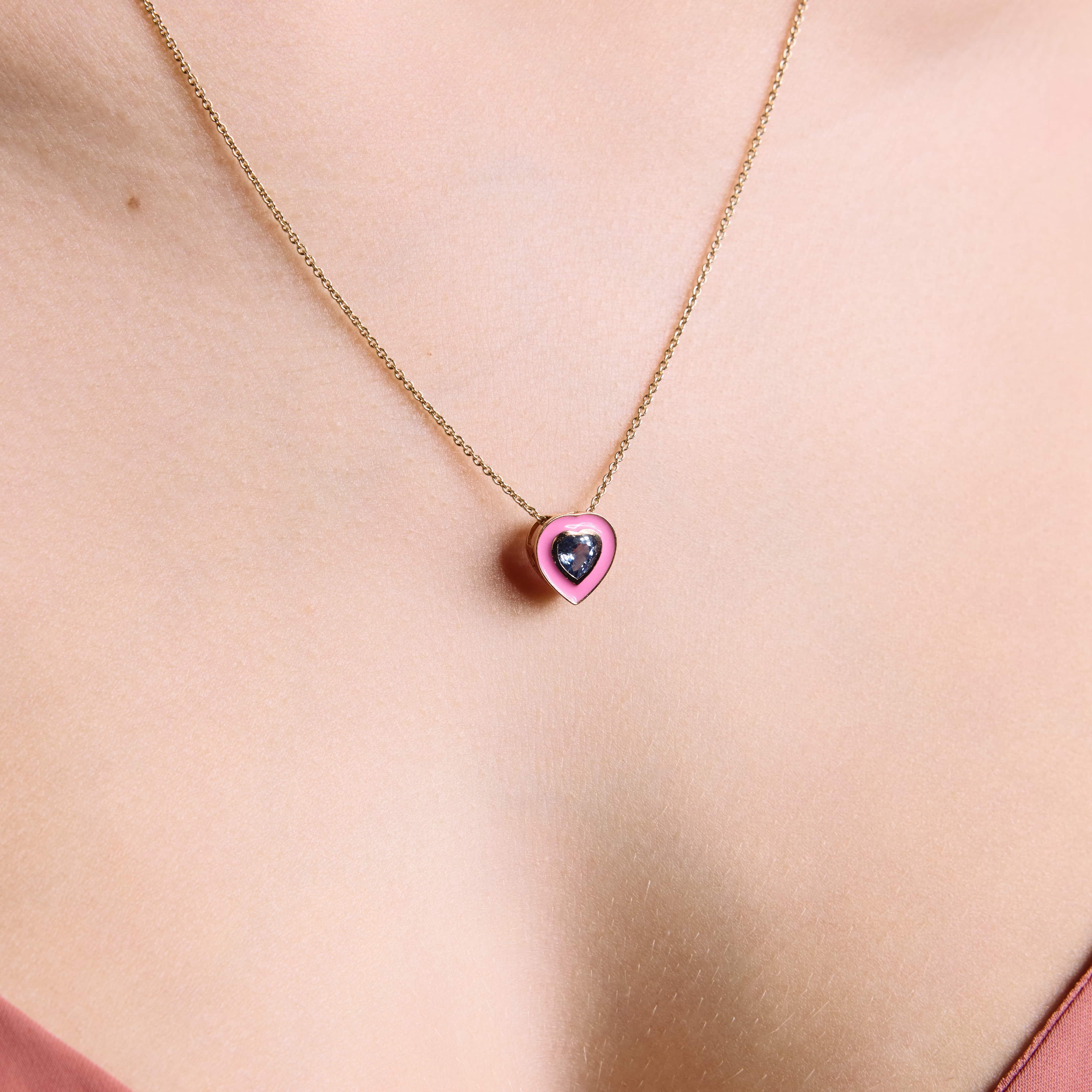 A close-up image of a person wearing a coloured enamel pendant, heart shaped, with a green sapphire heart in the middle