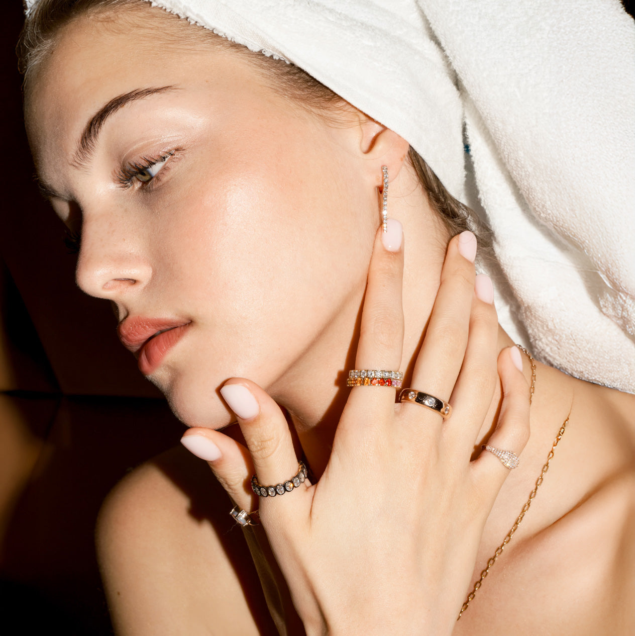 Woman wearing multiple gold and precious gemstones rings on her fingers with a towel on her head.