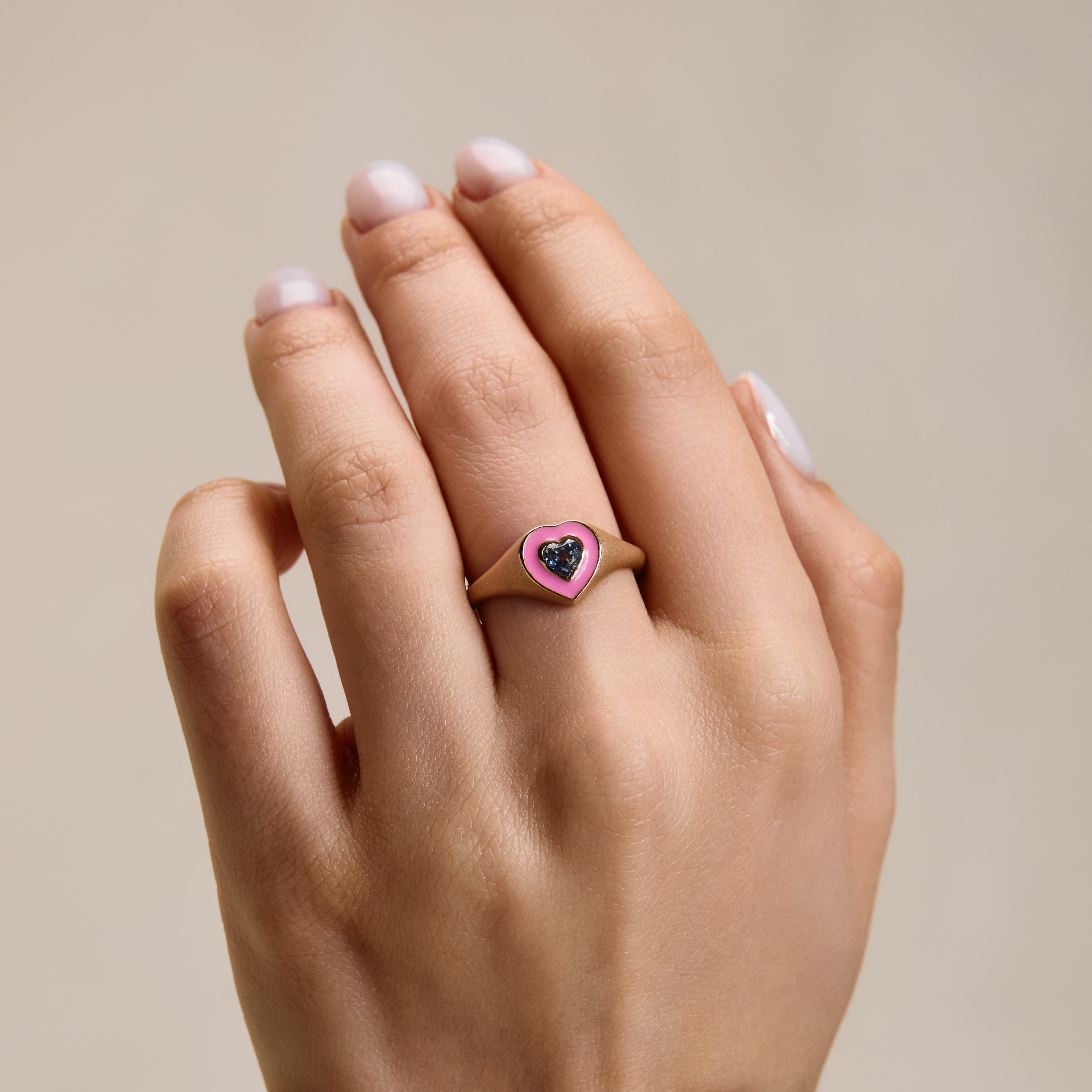 pink enamel ring with sapphire heart on hand