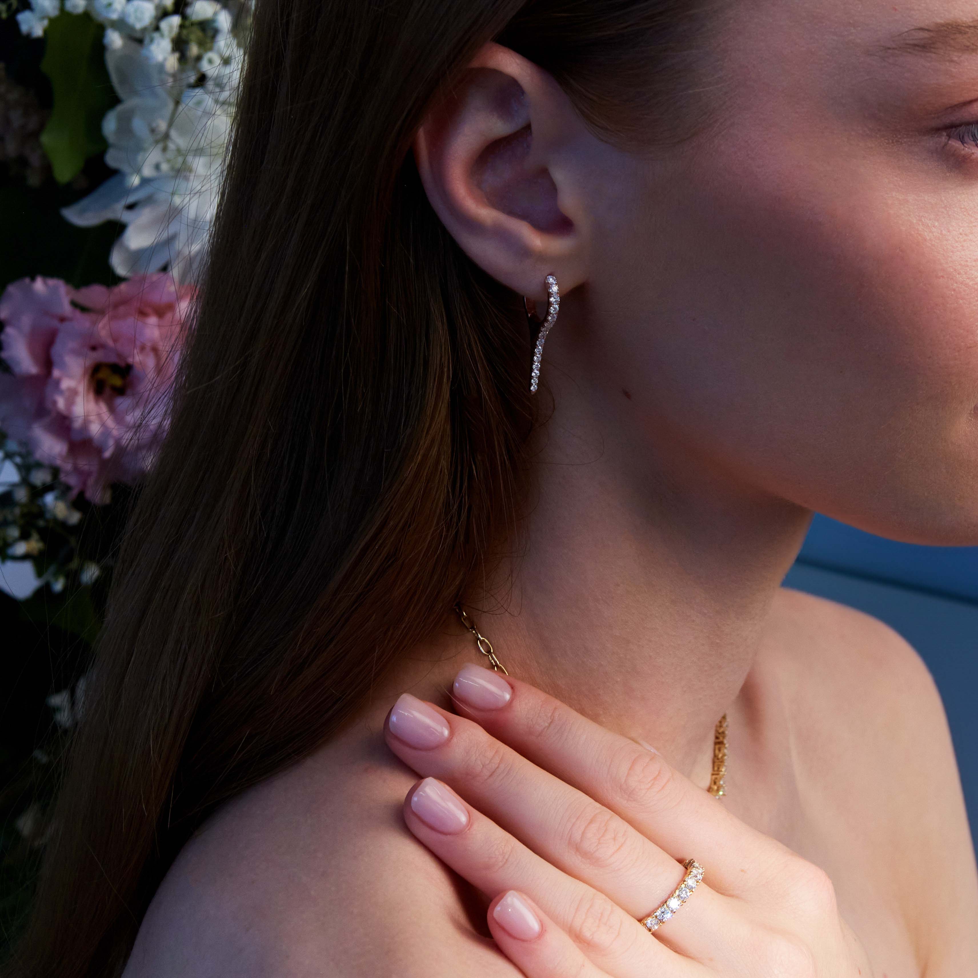 A pair of rose gold earrings with natural diamond drops, featuring a minimalist design on a ear.