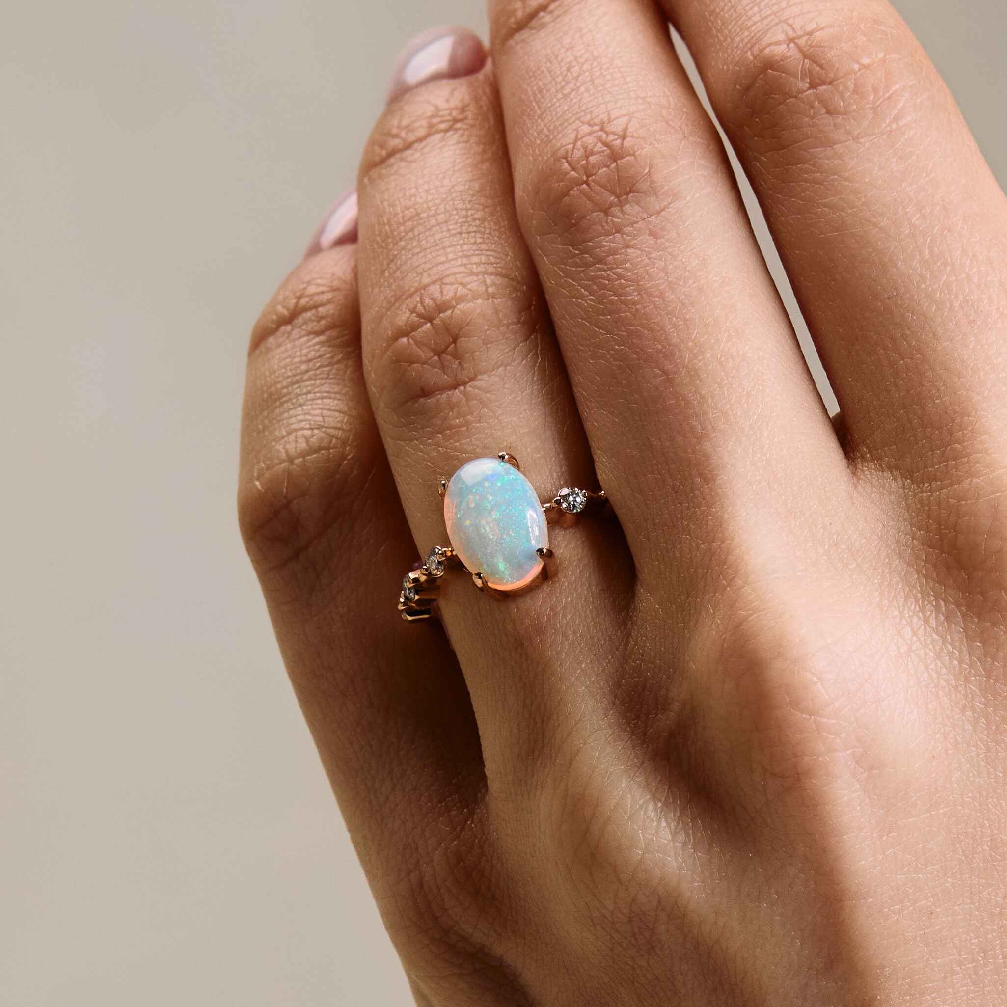 a gold ring with an opal center stone and white diamond accents on the band, on a hand