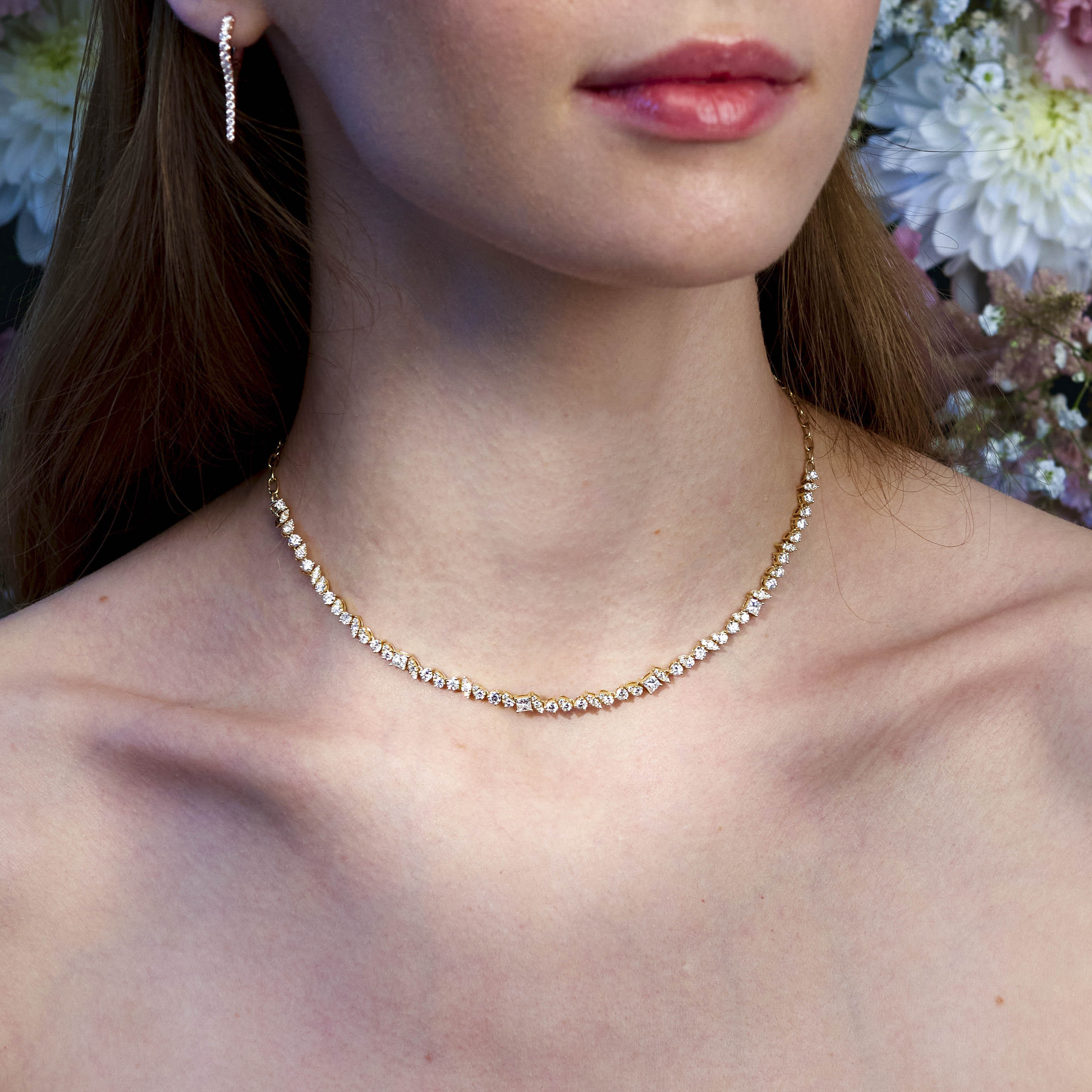 A girl wearing a tennis diamond tennis necklace with a floral background.