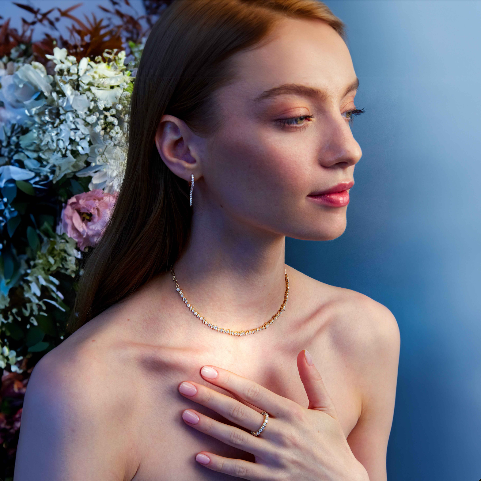 A beautiful woman wearing a tennis diamond tennis necklace and diamond earrings with a floral background.
