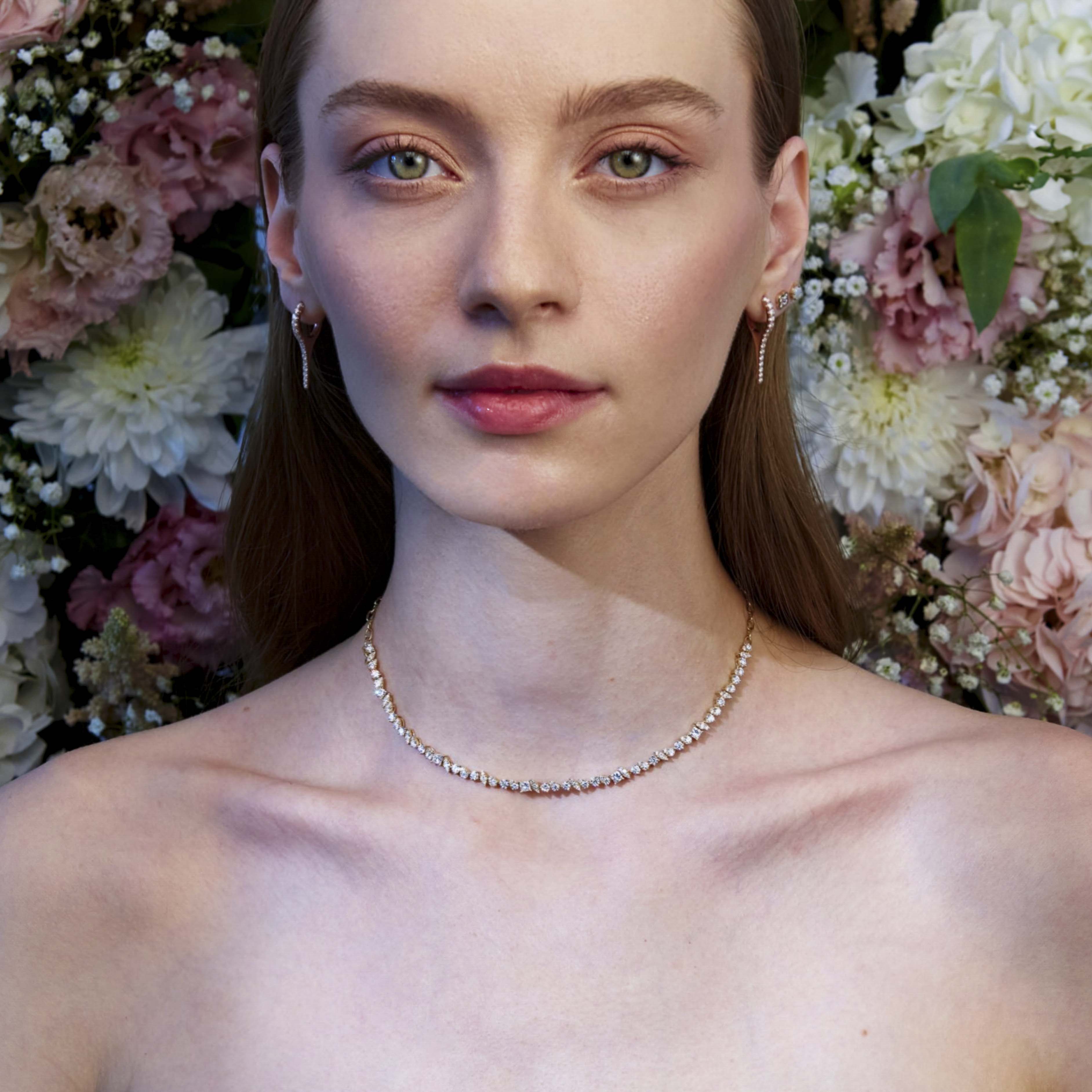 A girl wearing a tennis diamond tennis necklace and diamond earrings with a floral background.