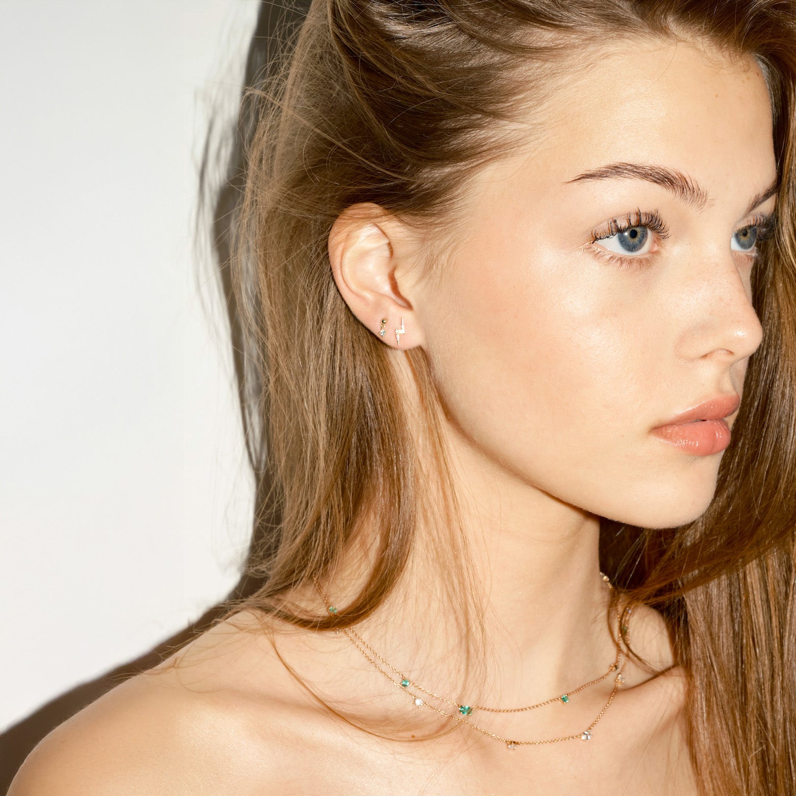 Close-up of a woman wearing a delicate necklace, and old lightning bolt earring with diamonds, on a plain background