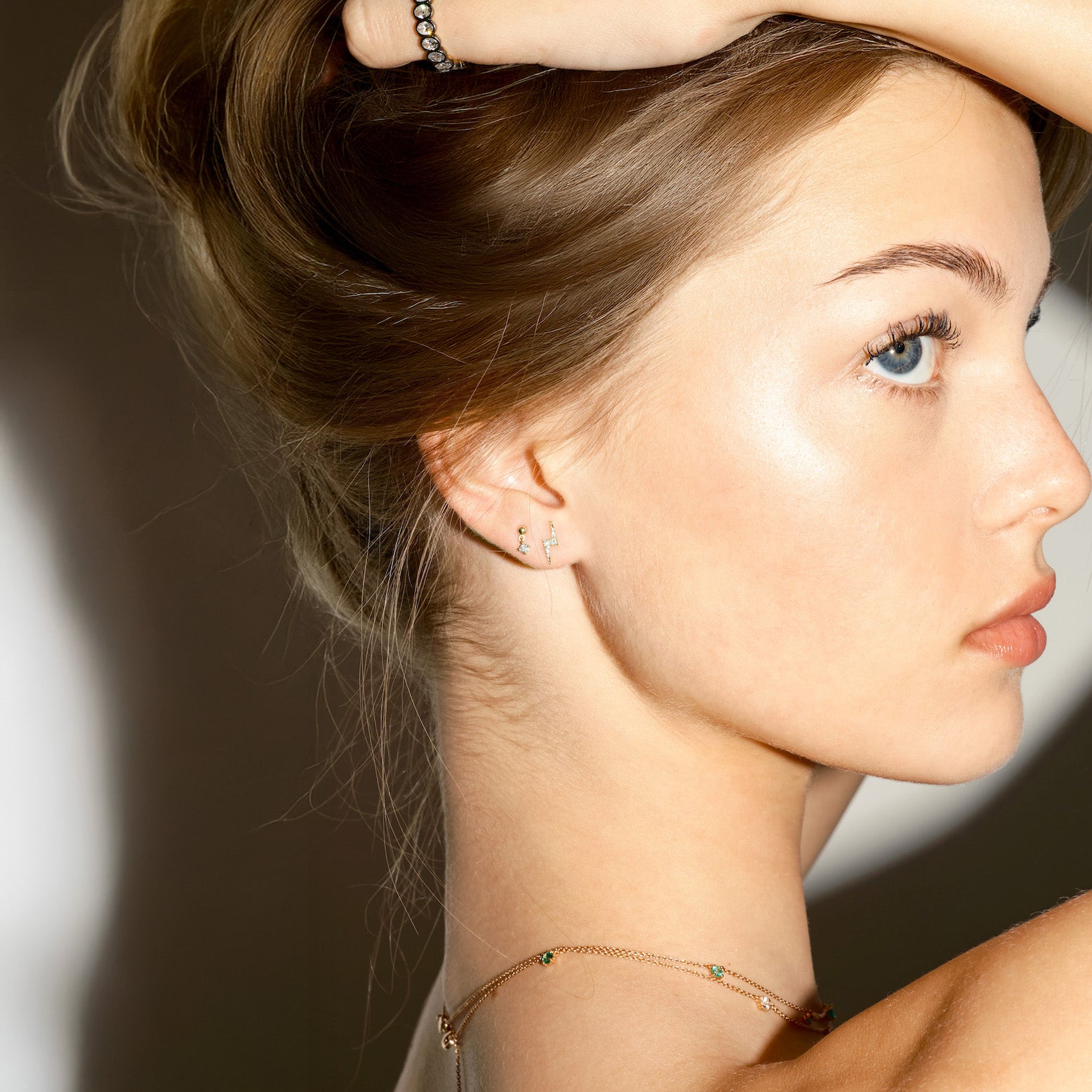 Close-up of a woman wearing gold lightning bolt, and floating dot earrings with diamonds, on a plain background