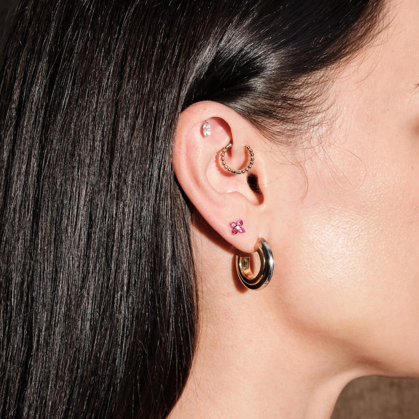 Close-up of an ear with gold hoop earrings, floating marquise diamond earring, and ruby studs on model's ear.