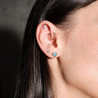 Close-up of an ear with multiple earrings, floating marquise diamond, beaded hoop, diamonds triangle stud, australian opal and diamonds heart studs, on a dark background