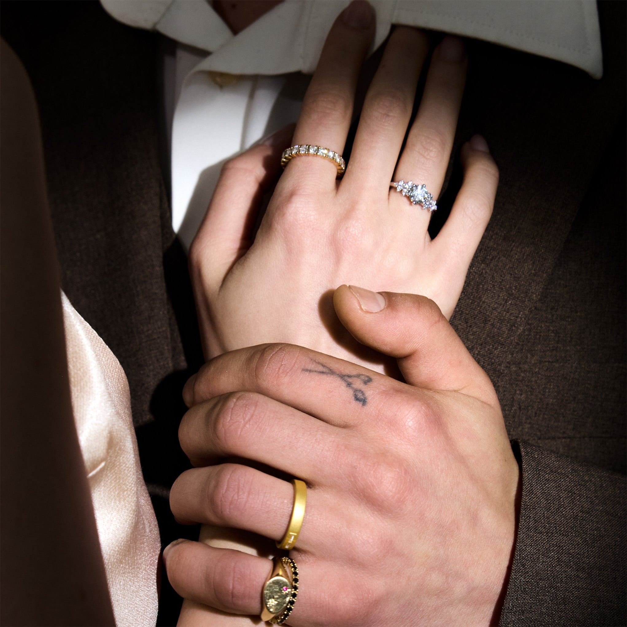 Close-up of two people holding hands with visible jewelry, morse code wedding band, eternity diamond ring, garden on eden diamond ring. 