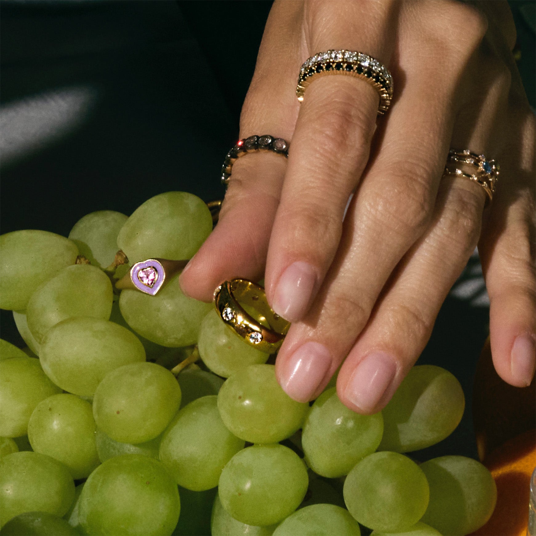 Hand with multiple gold and diamonds rings on a bunch of green grapes