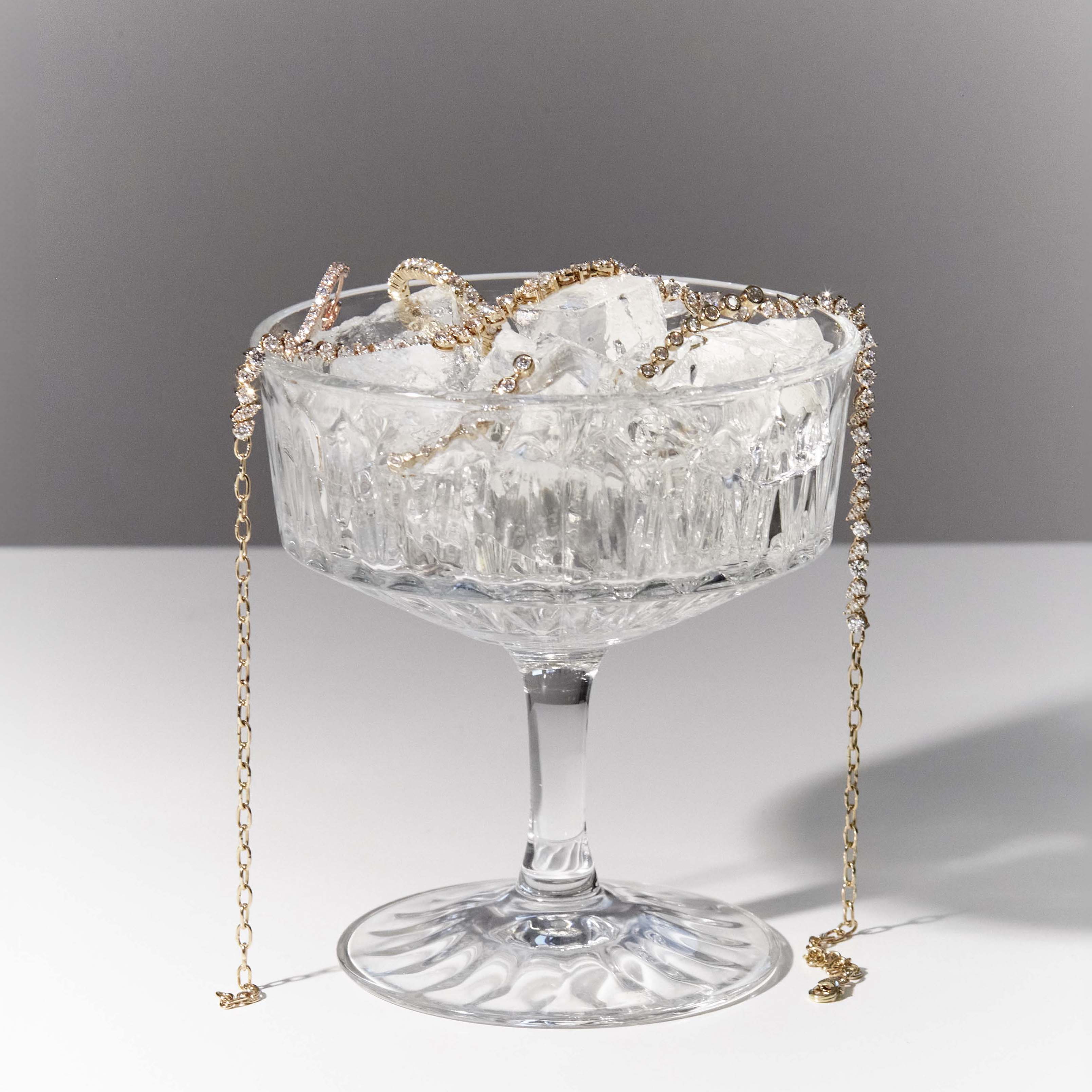 a glass full of of ice and diamond jewelry, earrings, tennis diamond ring and tennis diamond choker