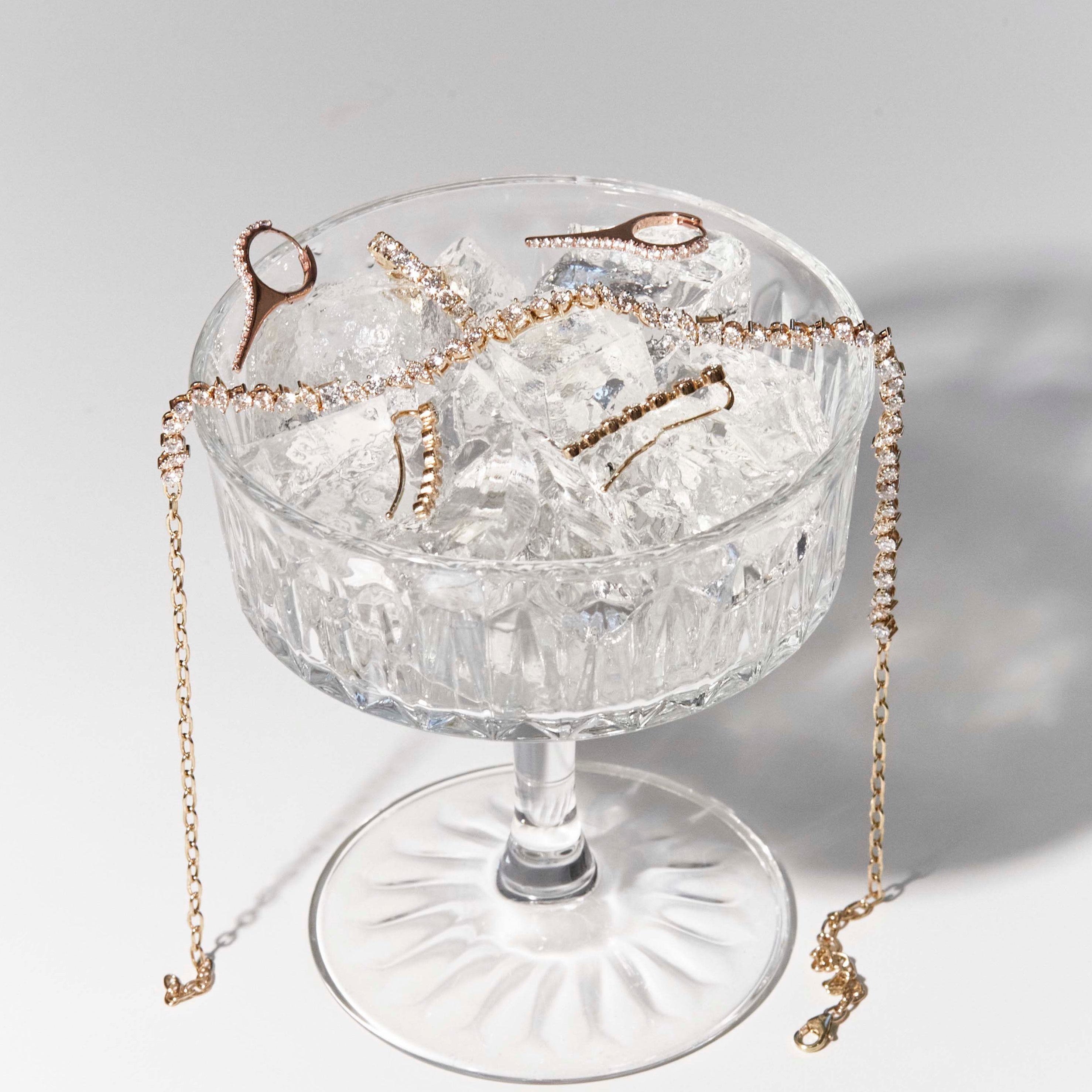 A cocktail glass with the perfect brew in it, diamond jewellery of all sorts on ice, earrings, choker and a eternity ring. 
Un pahar de cocktail care conține băutura perfectă, bijuterii cu diamante de tot felul, cercei, choker și un inel eternity. 