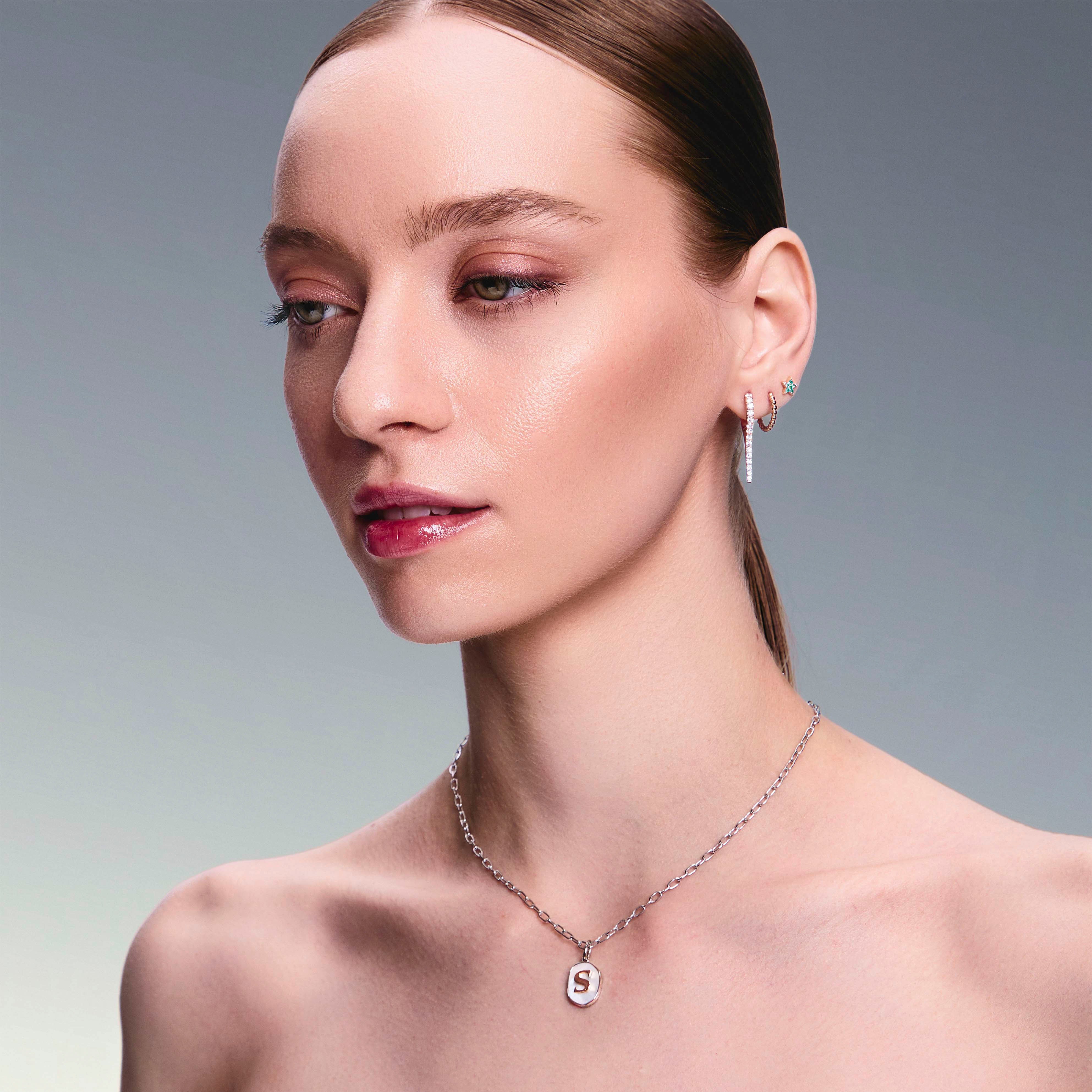beautiful model wearing a mother of pearl pendant with a gold letter, diamonds drops earrings, gold hoops and star studs earrings. 