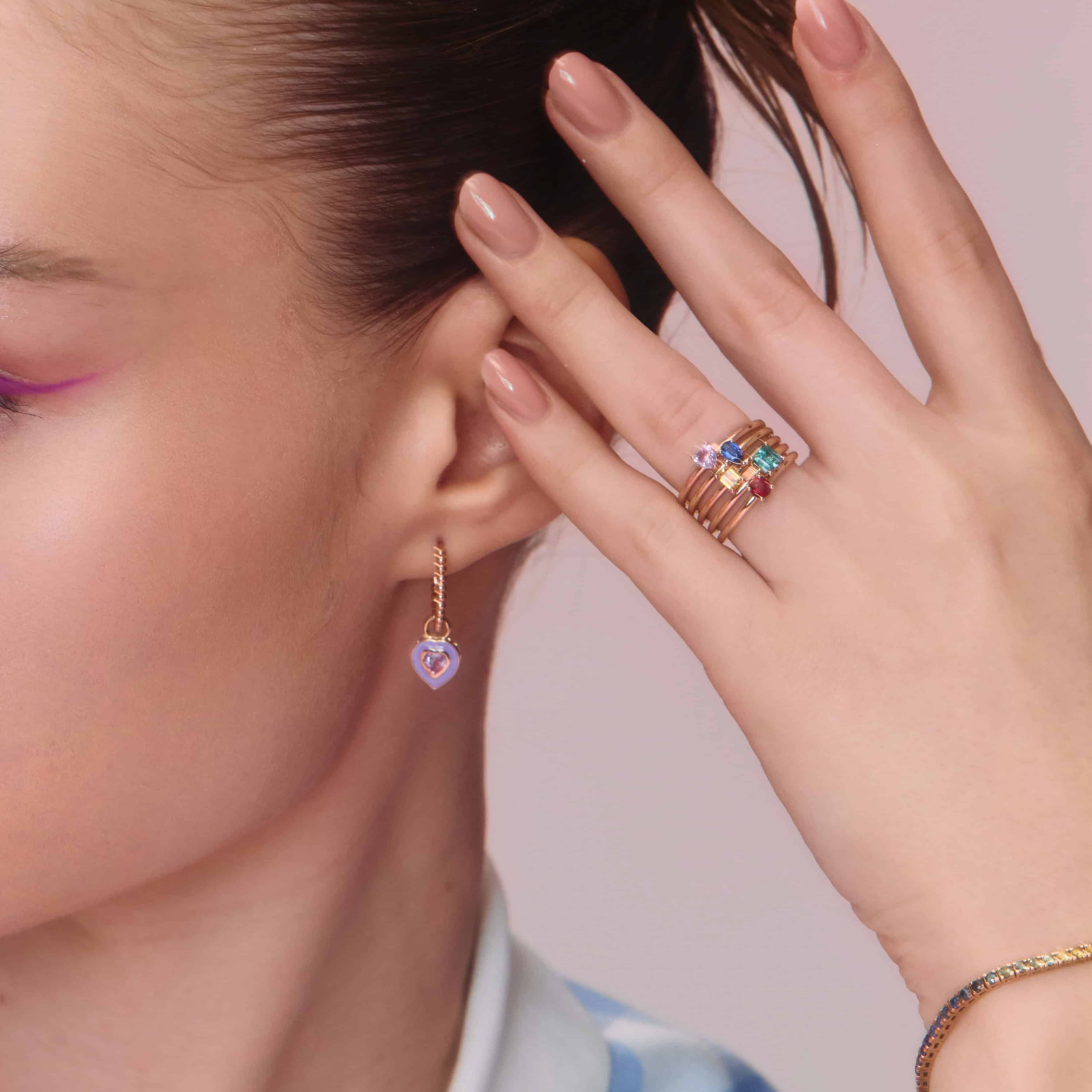 A collection of gold rings with a central ruby stone, accompanied by smaller multicolored stones, stacked on a person's finger.
