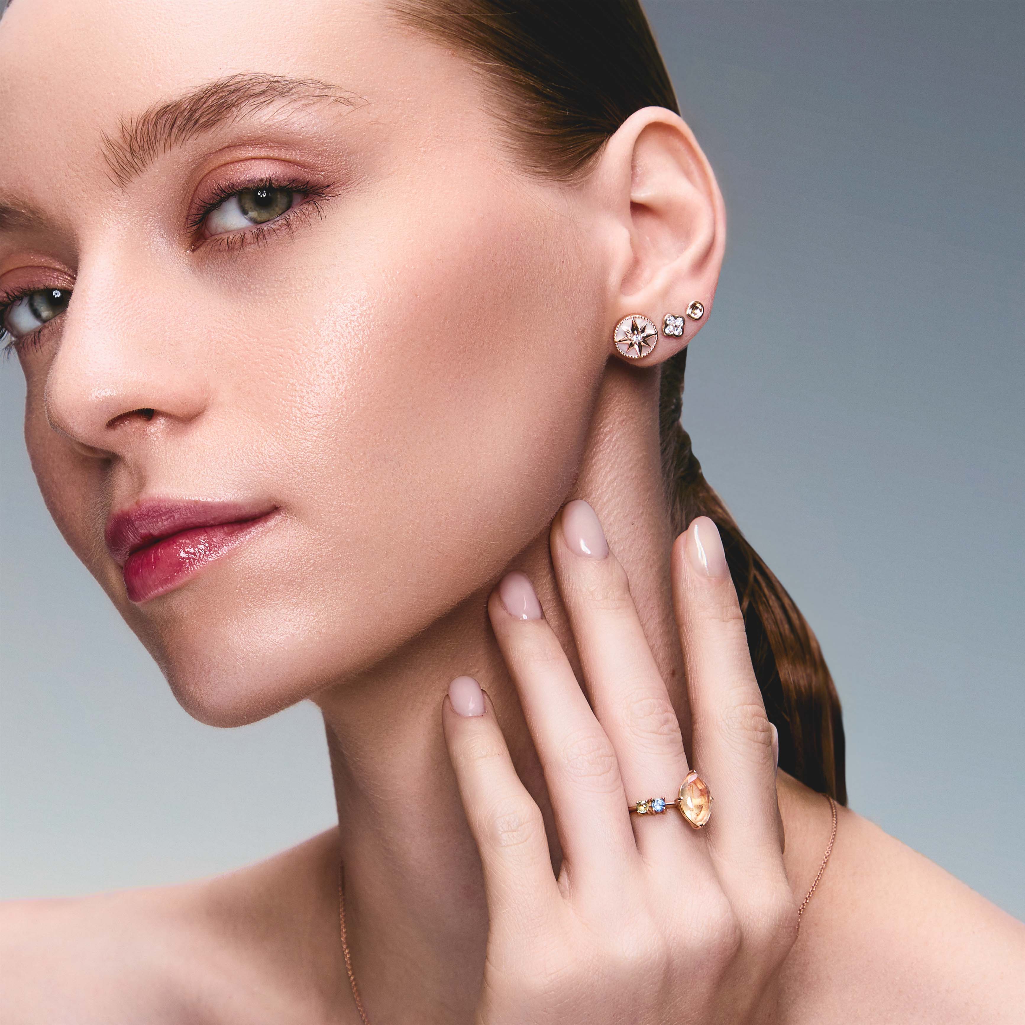 A pair of gold studs earrings with a simple design, resembling a prayer bowl or birds' nest, a clover diamonds earring, a mother of pearl lodestar earring, on an ear.