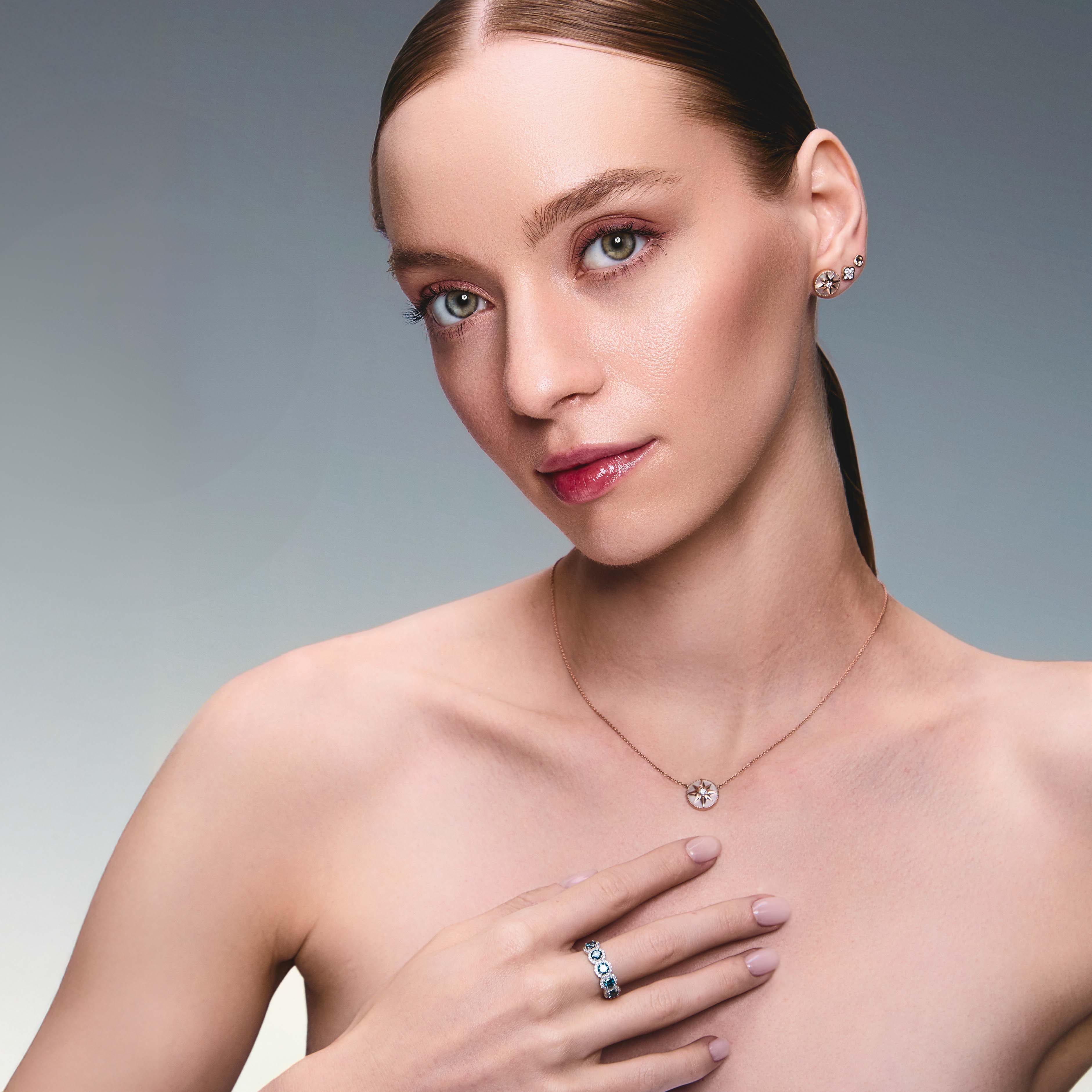 A pair of gold studs earrings with a simple design, resembling a prayer bowl or birds' nest, a clover diamonds earring, a mother of pearl lodestar earring, Lodestar Necklace and blue diamonds half eternity ring on model.