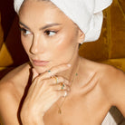Woman with a towel on her head, wearing jewelry, rings with diamonds and colourful precious stones, in a warm-toned setting