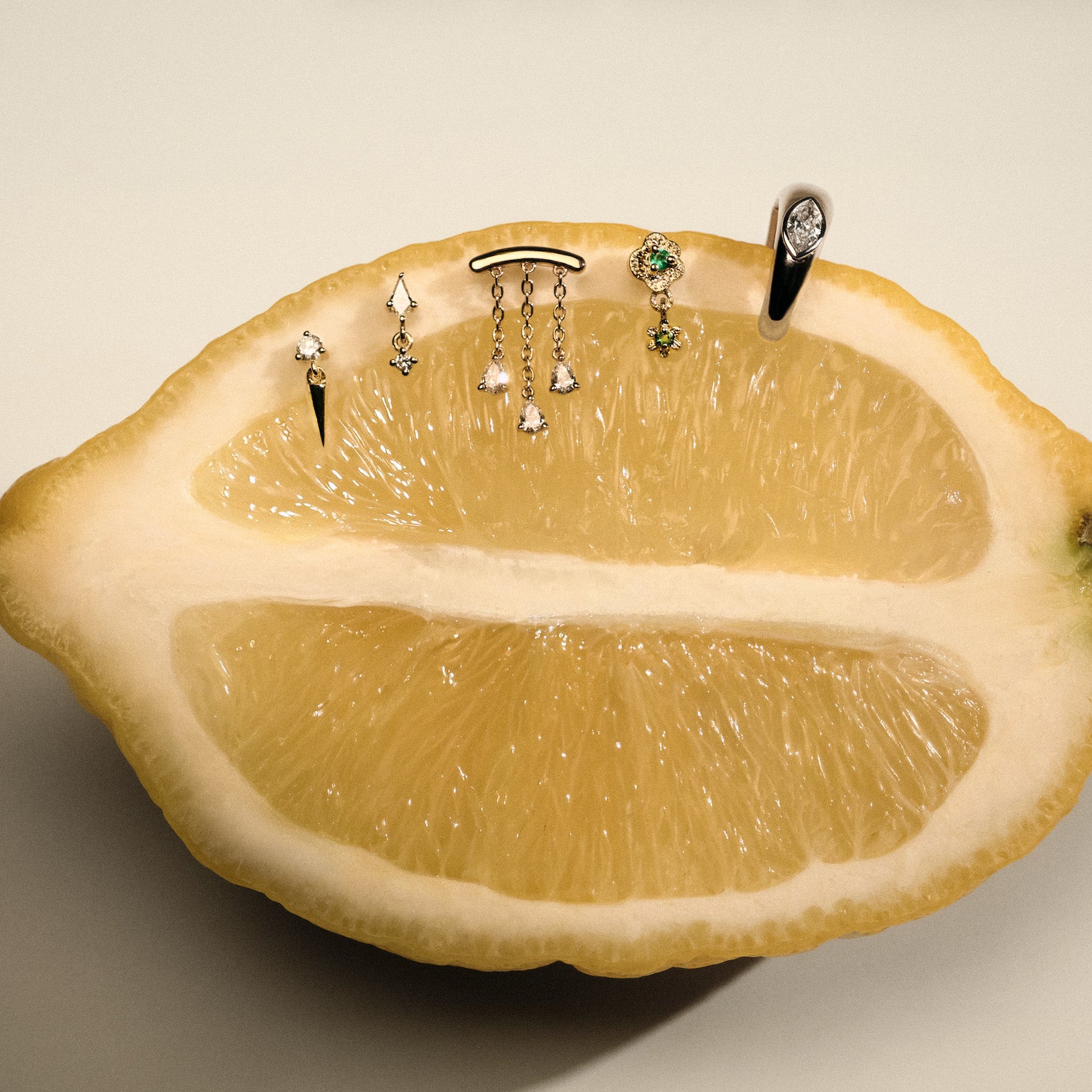 Gold earrings, Teardrop Diamonds Chandelier stud, The Floating Kite Diamond Stud, The Floating Gold Icicle Stud, The Marquise Earcuff, The Wild Rose Stud with Emerald on a lemon with a neutral backgrounda.