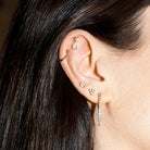 Close-up of an ear with multiple gold and diamonds earrings against a neutral background