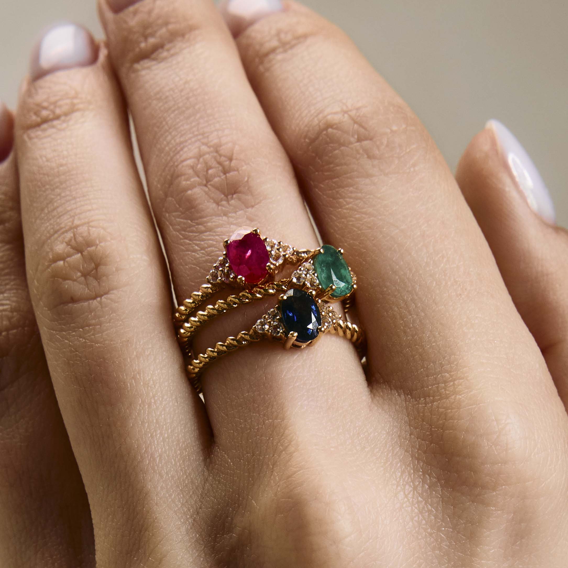 elegant oval blue sapphire ring, oval ruby ring and oval emerald ring with diamonds side cluster and a twisted band stacked on hand 