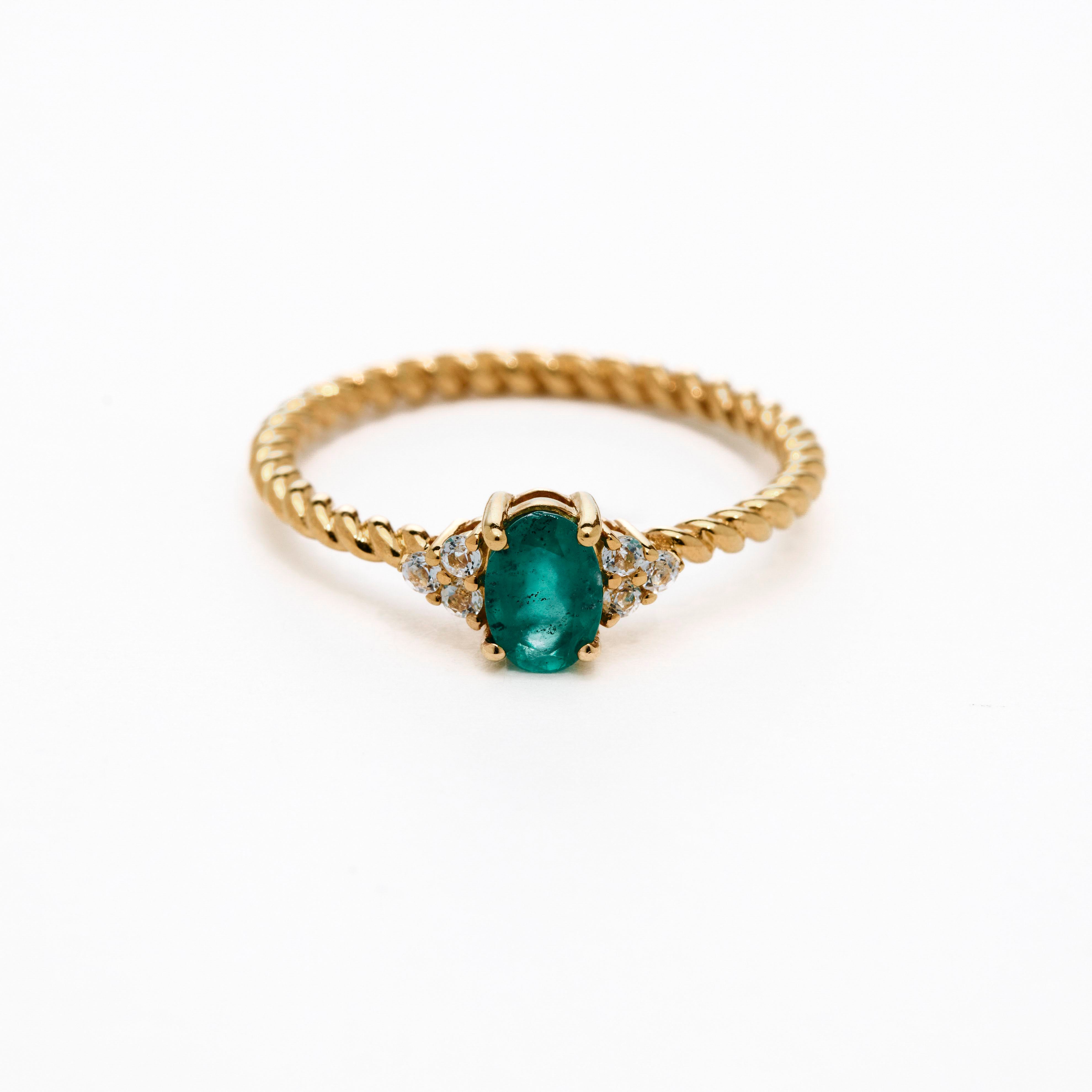 A rose gold ring featuring a central emerald stone flanked by white diamonds on either side, set against a white background.