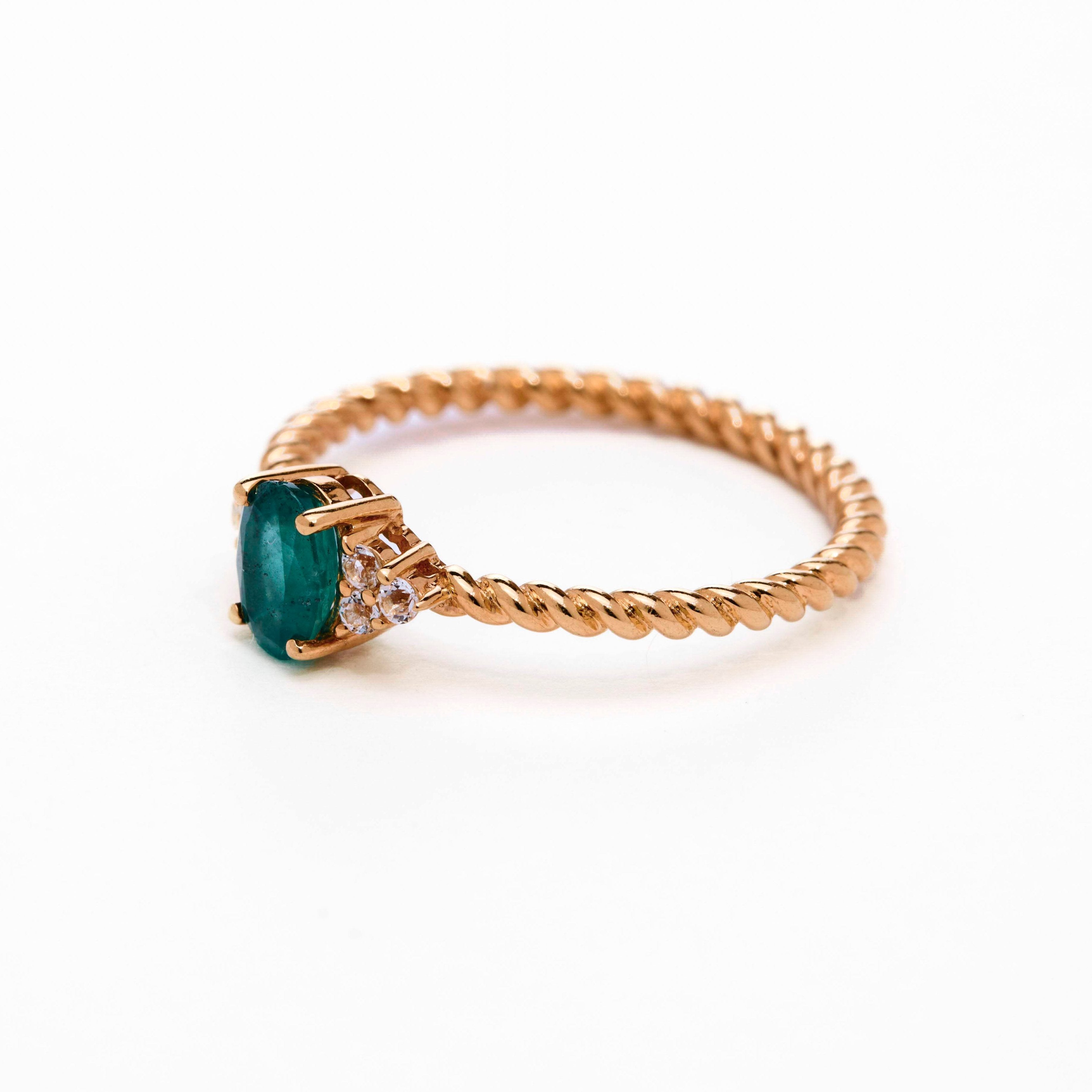 A rose gold ring featuring a central emerald stone flanked by white diamonds on either side, set against a white background.