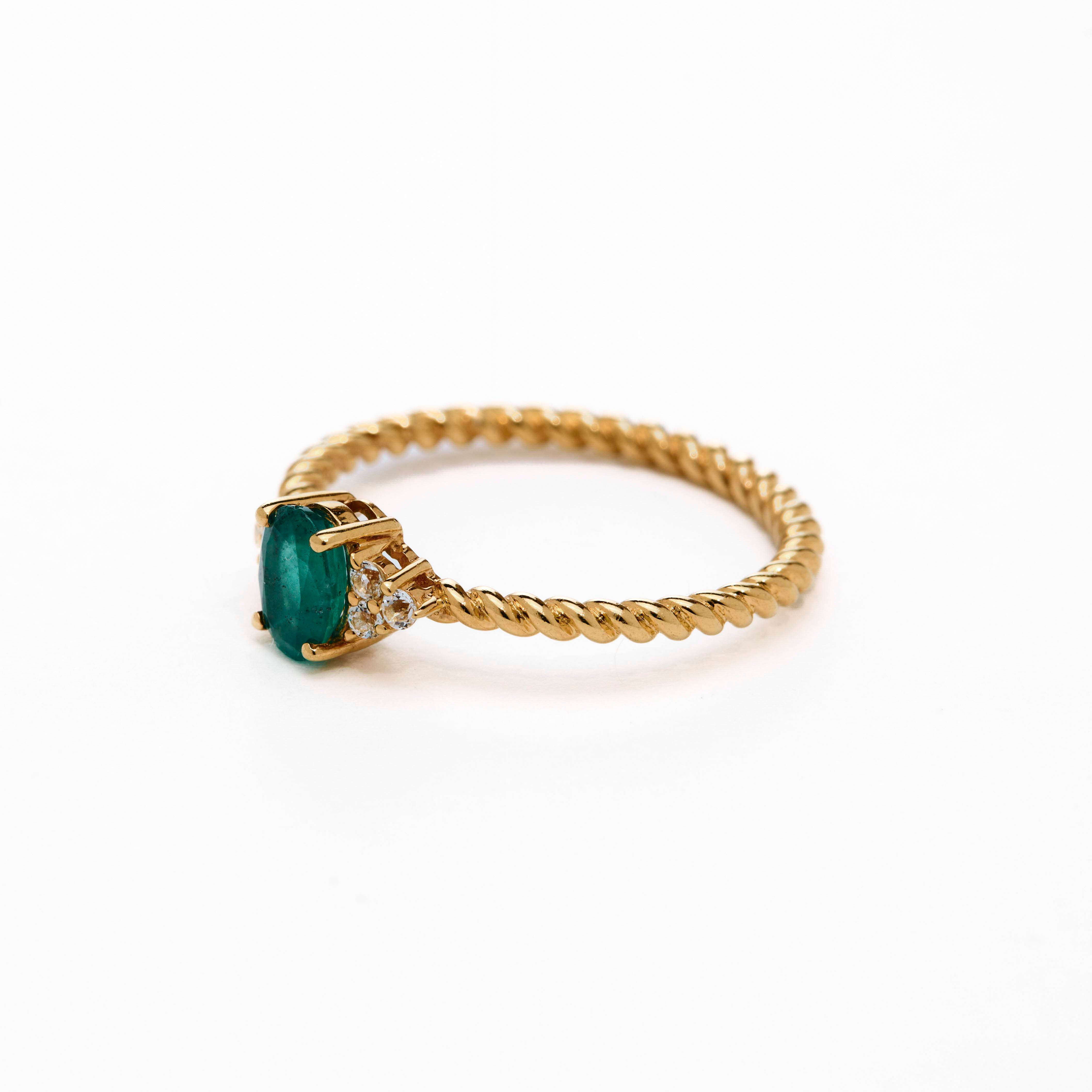 A rose gold ring featuring a central emerald stone flanked by white diamonds on either side, set against a white background.