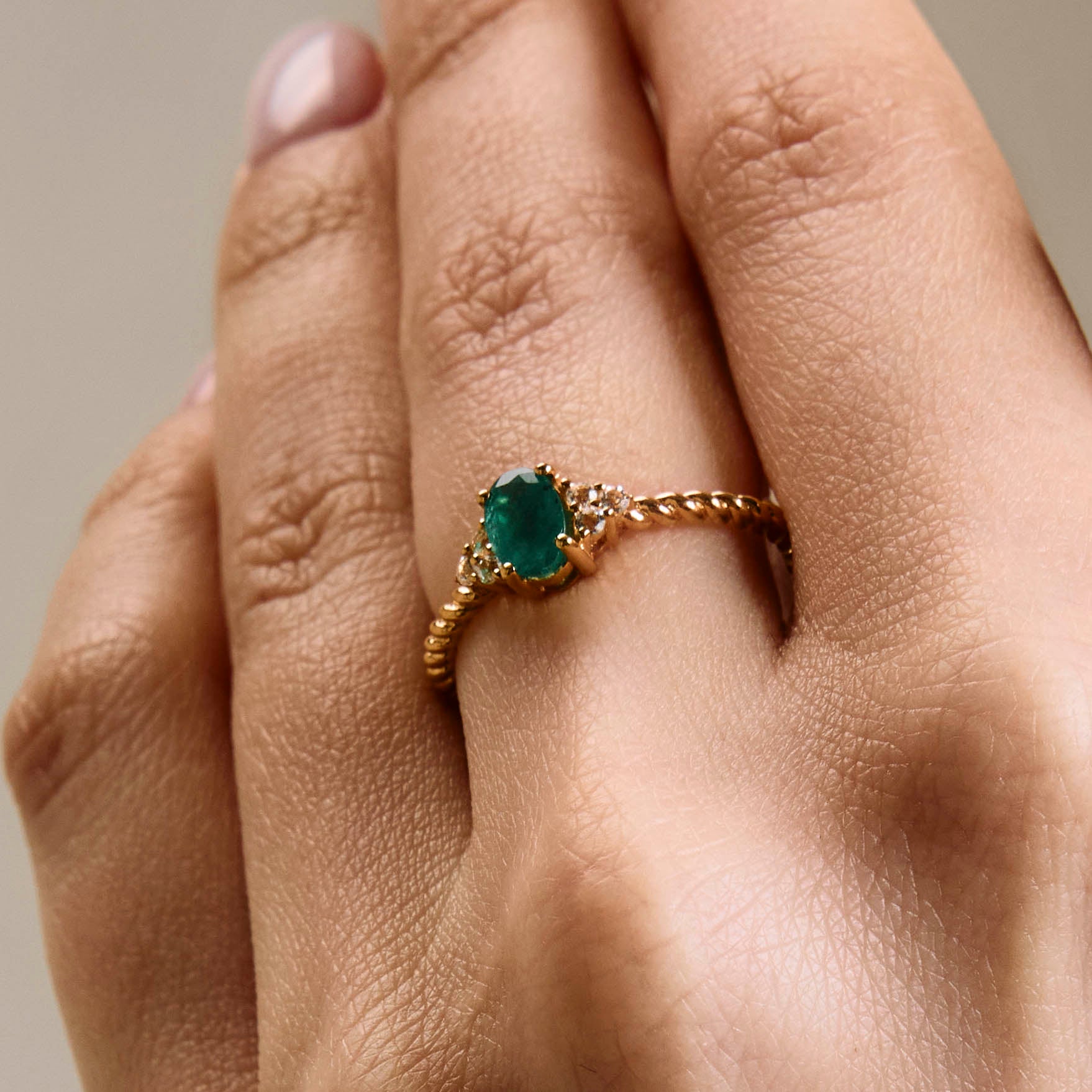 A rose gold ring featuring a central emerald stone flanked by white diamonds on either side, on hand