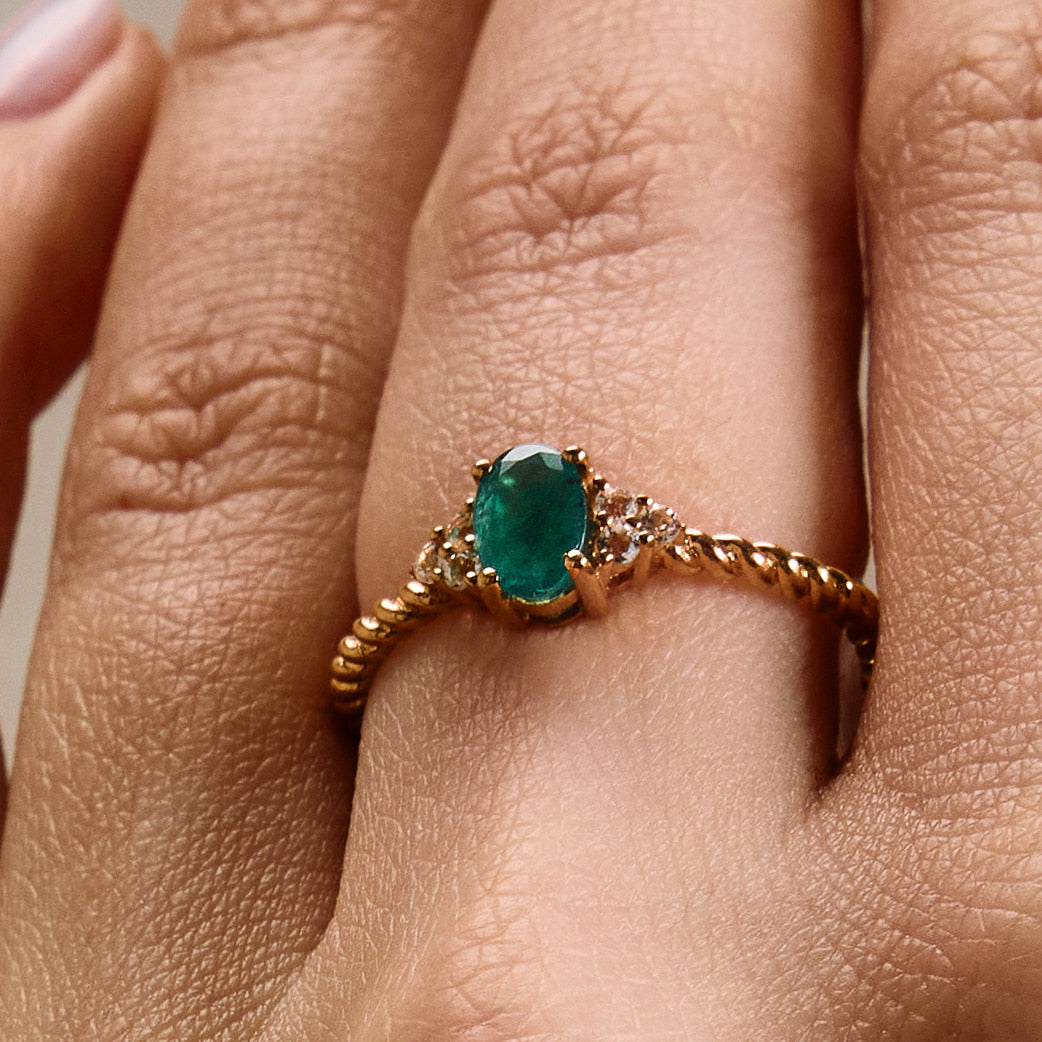 A rose gold ring featuring a central emerald stone flanked by white diamonds on either side, on finger