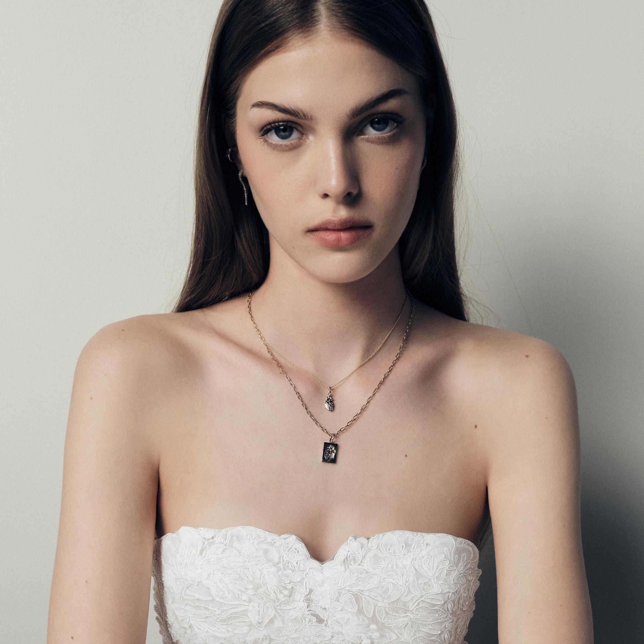 Woman wearing a strapless white lace dress with jewelry, a necklace with 14k gold heart plates on a neutral background