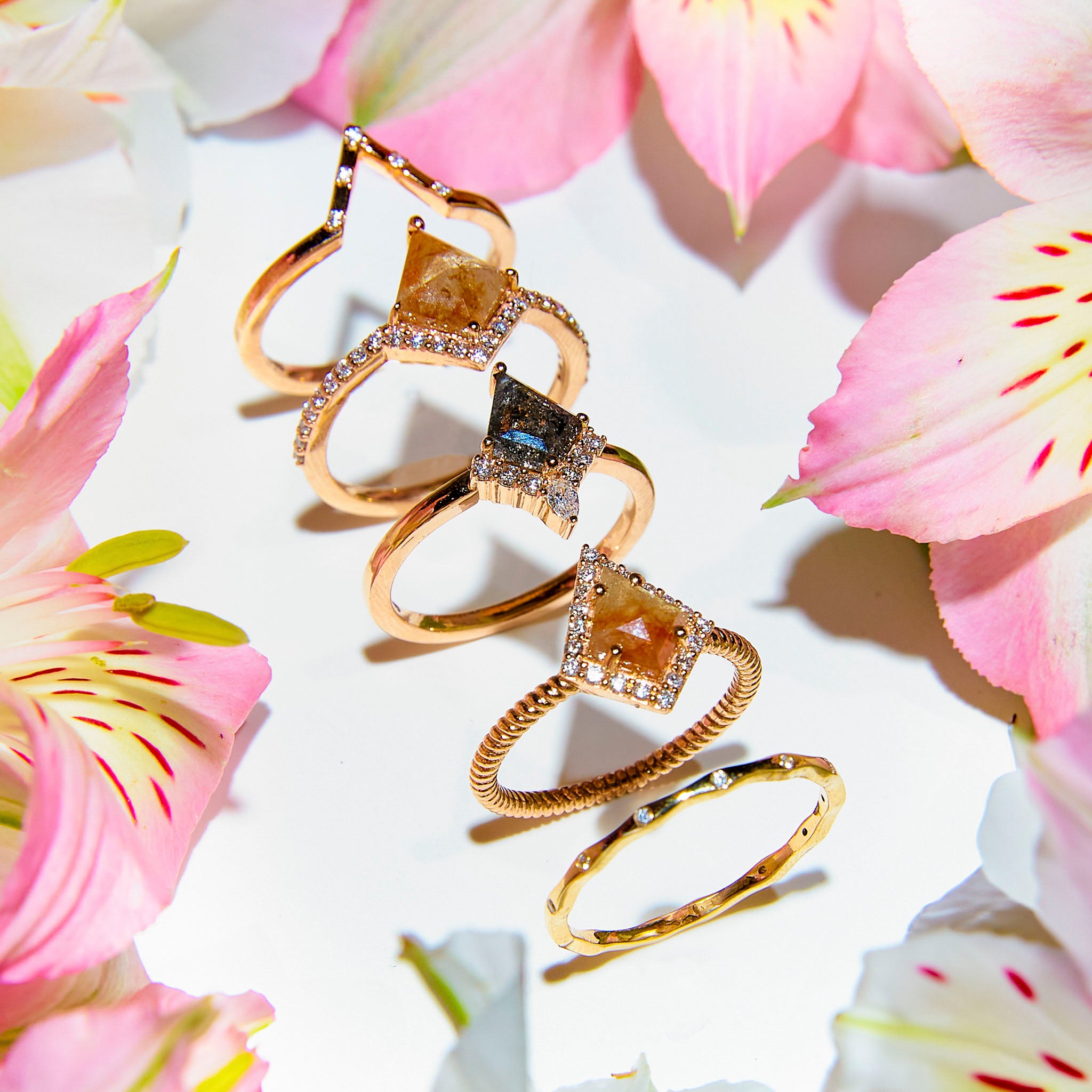 a collection of rings,  with kite shaped salt and pepper diamonds and white diamonds in different gold tones 