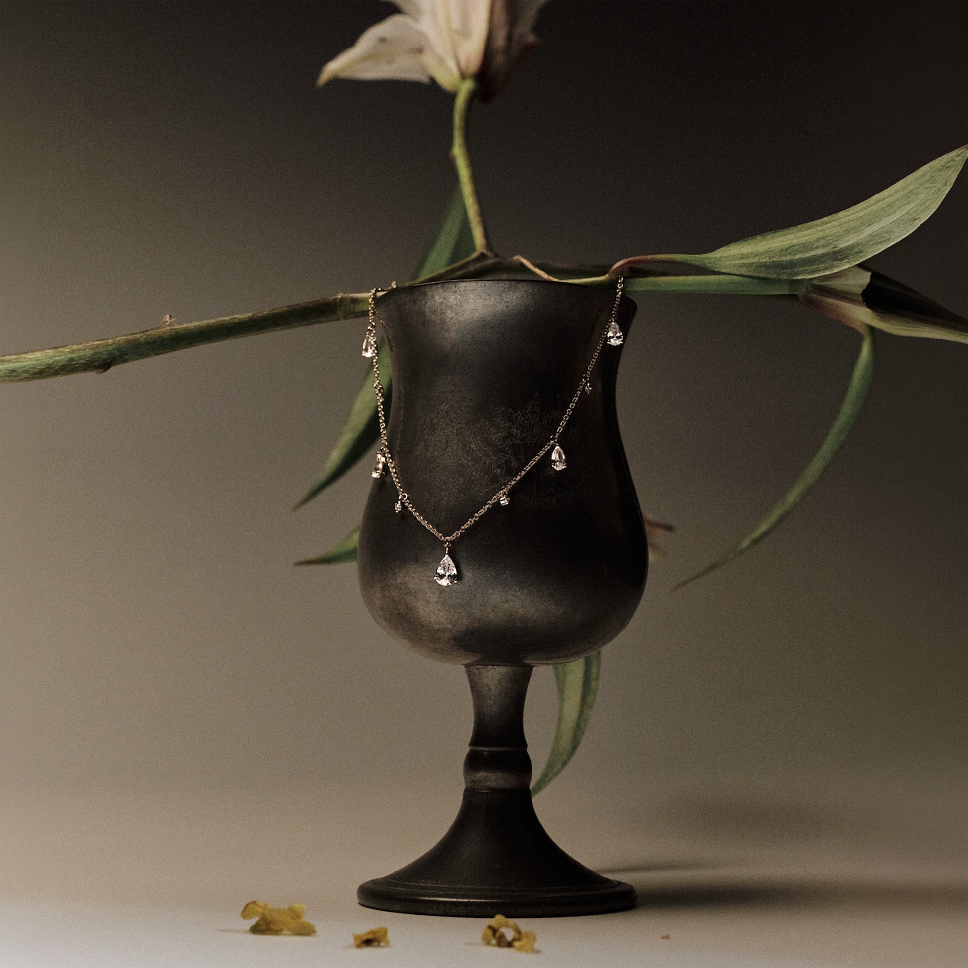 Gold Necklace with teardrop and round diamonds pendants on a black stand with green leaves in the background.